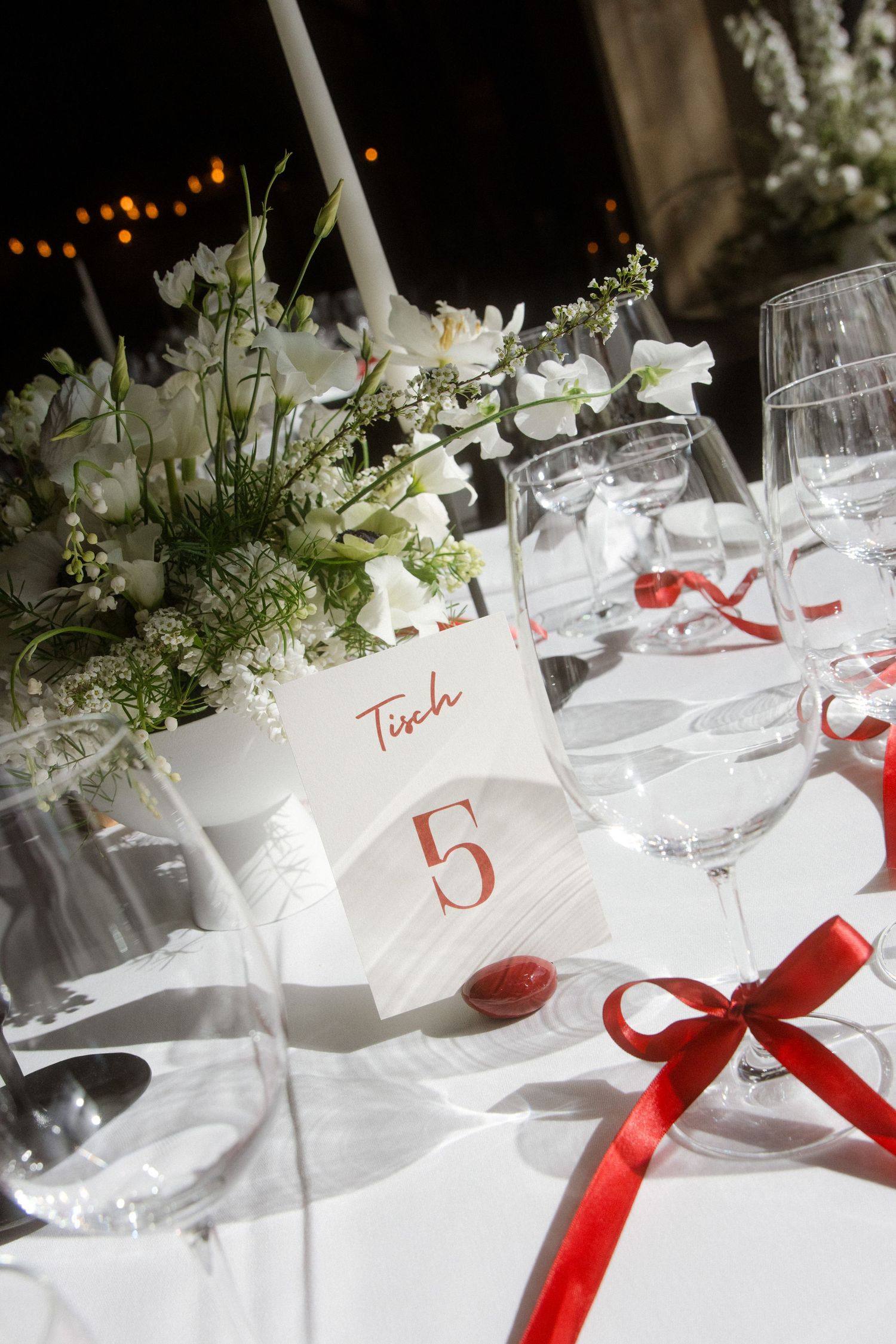 Elegant wedding table setting with white flowers, candle, wine glasses, and red ribbon accents at Table 5.