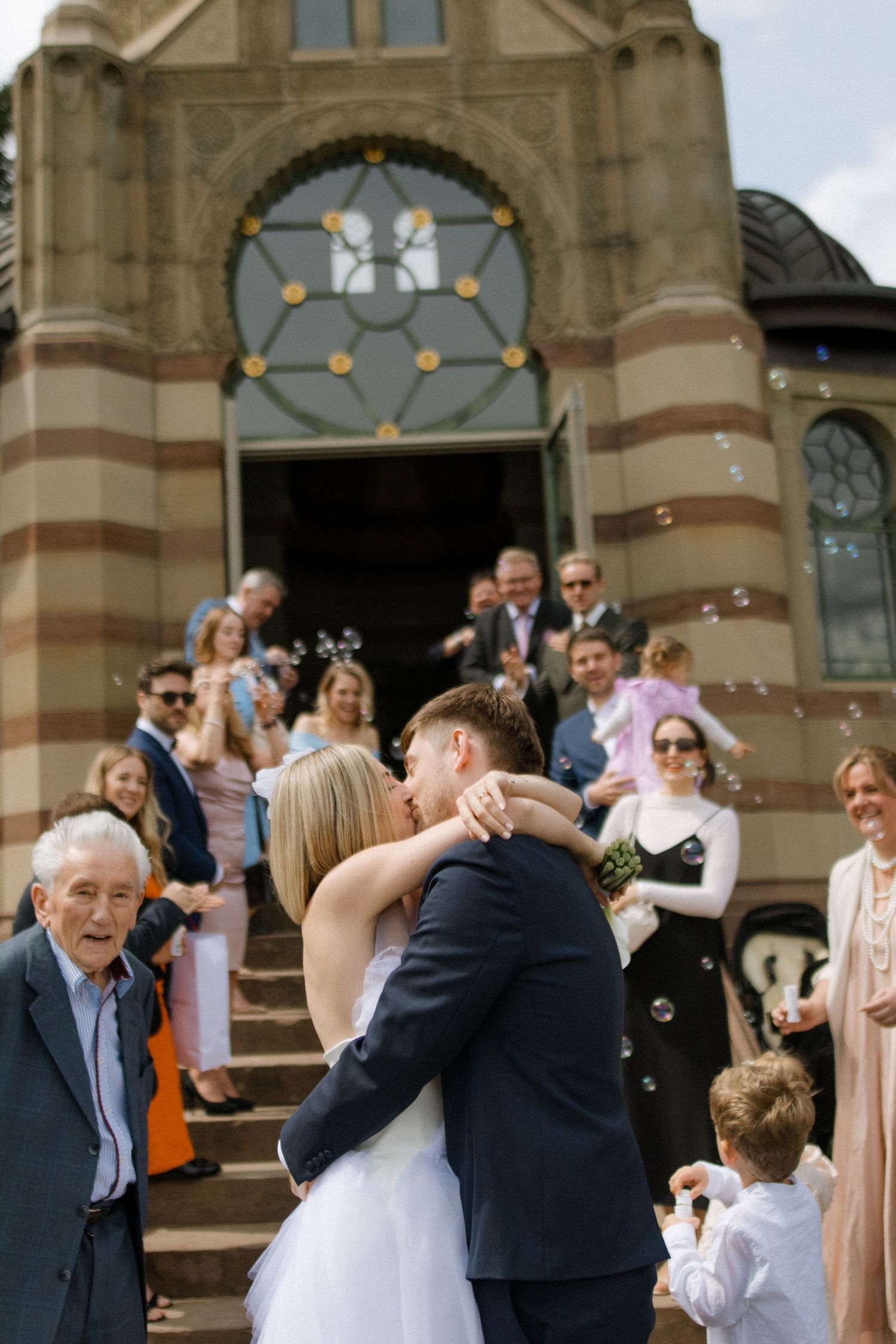Wedding guests throwing confetti as the newlyweds exit a historic stone church building.