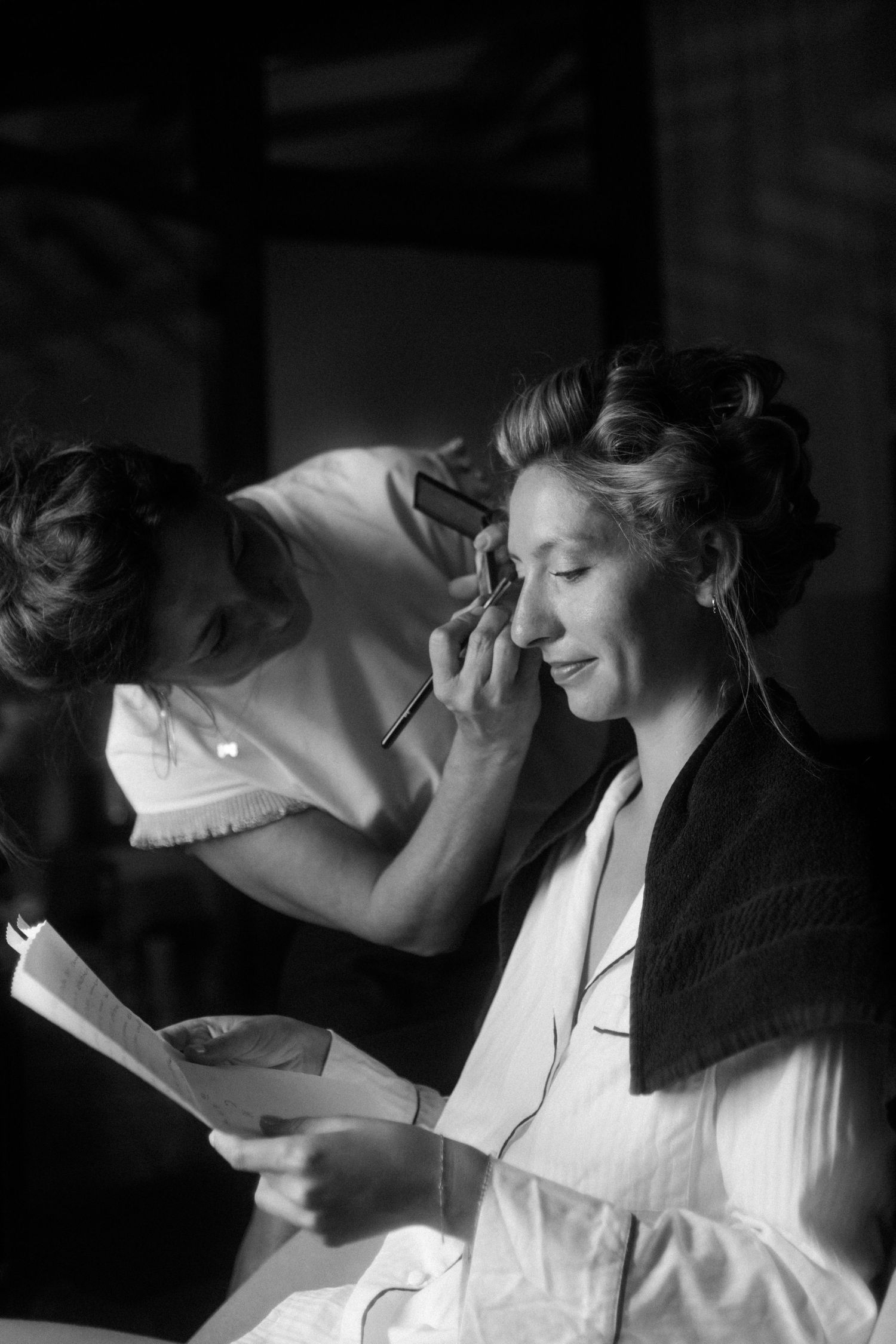 Black and white photo of wedding preparation with makeup being applied.