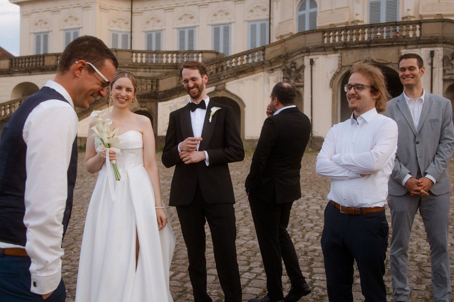 Wedding party gathered outside a grand historic building with ornate architecture.
