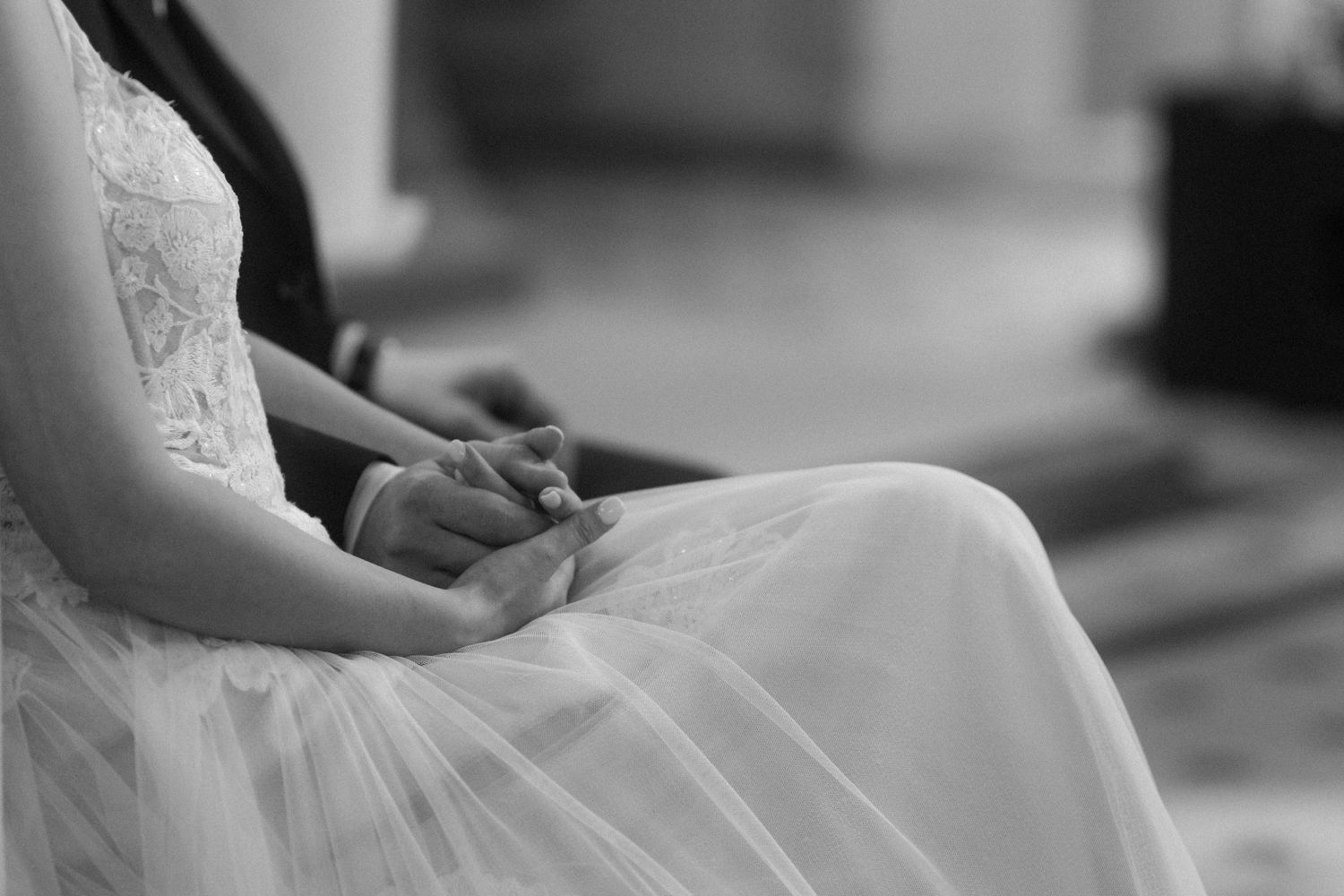 Close-up black and white shot of hands resting on a white lace wedding dress.