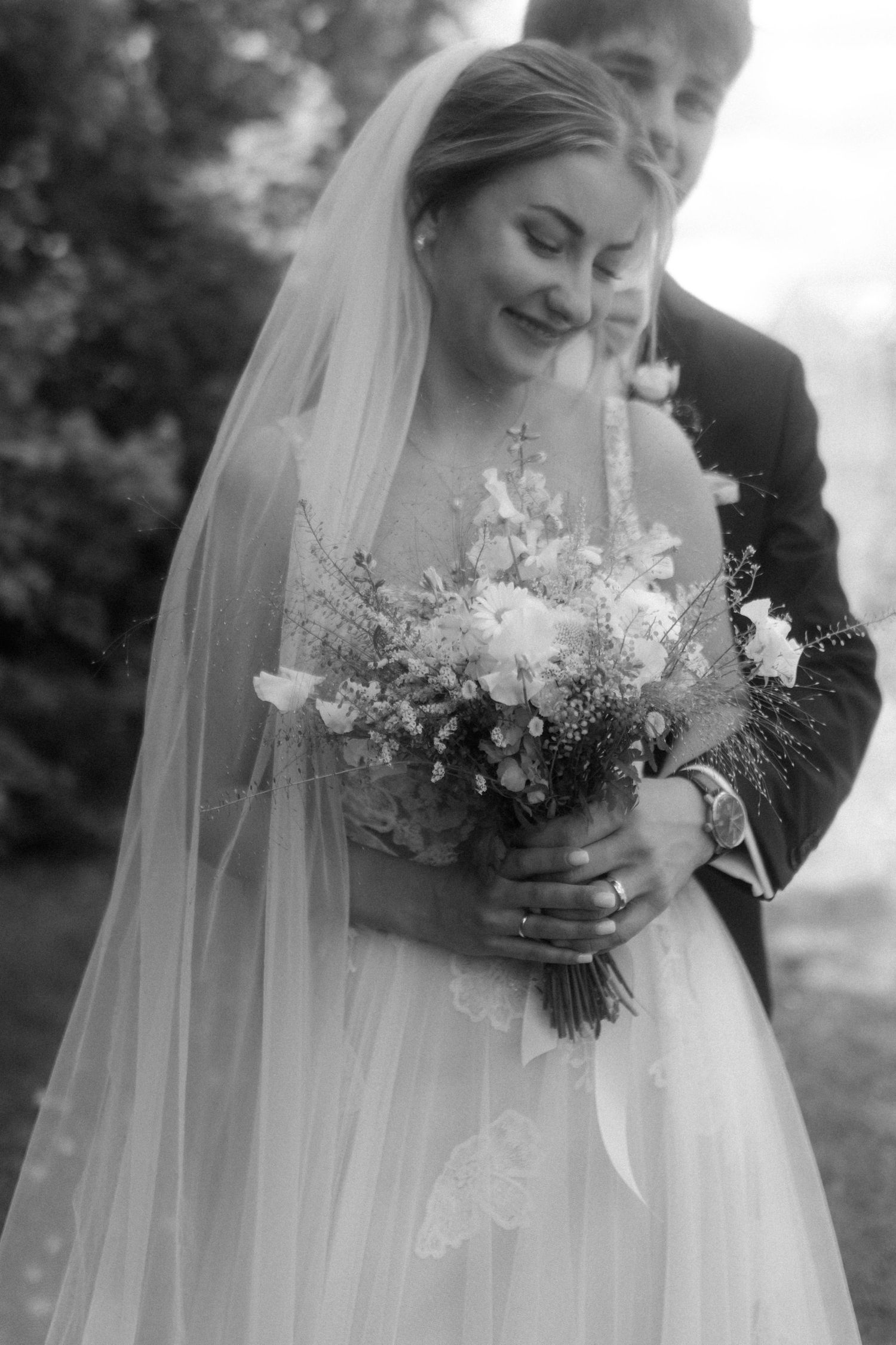 Black and white intimate portrait showing tender wedding moment with detailed view of floral bouquet.