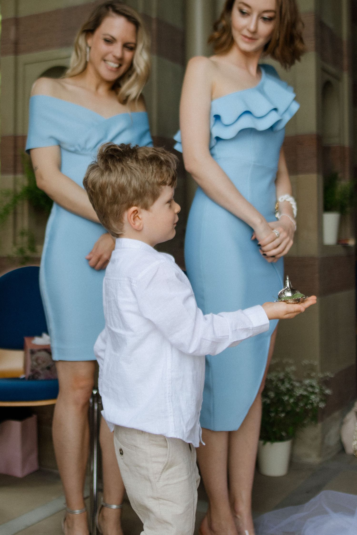 Young ring bearer in white shirt standing between bridesmaids in light blue dresses.