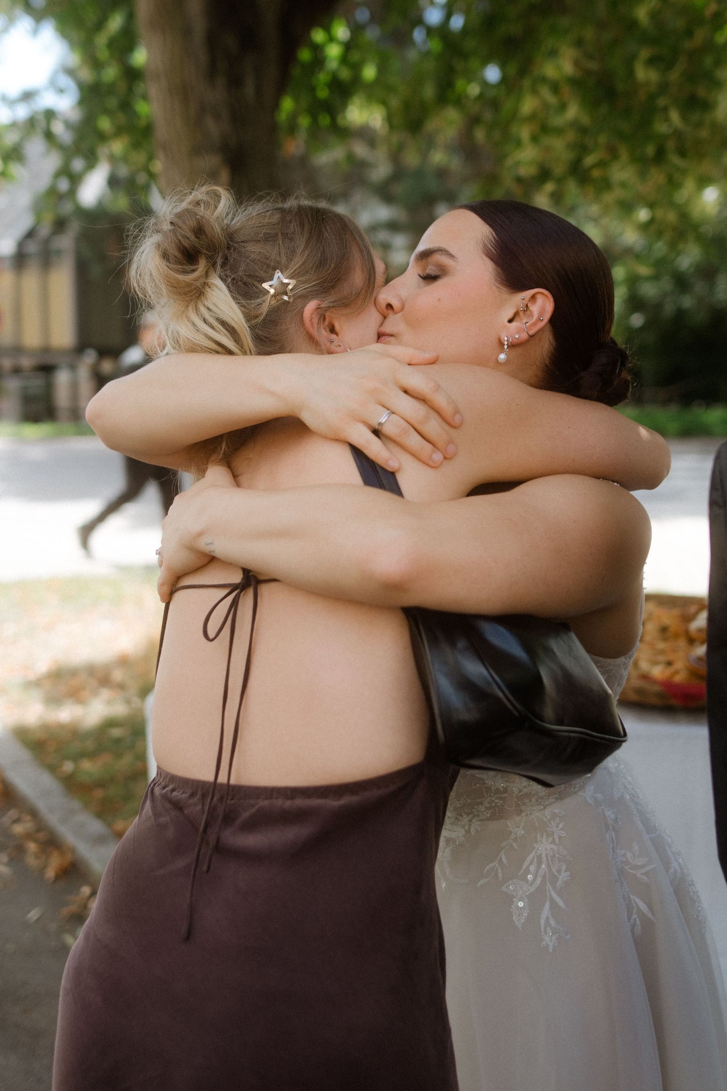 Two friends share an emotional embrace at a wedding celebration outdoors.