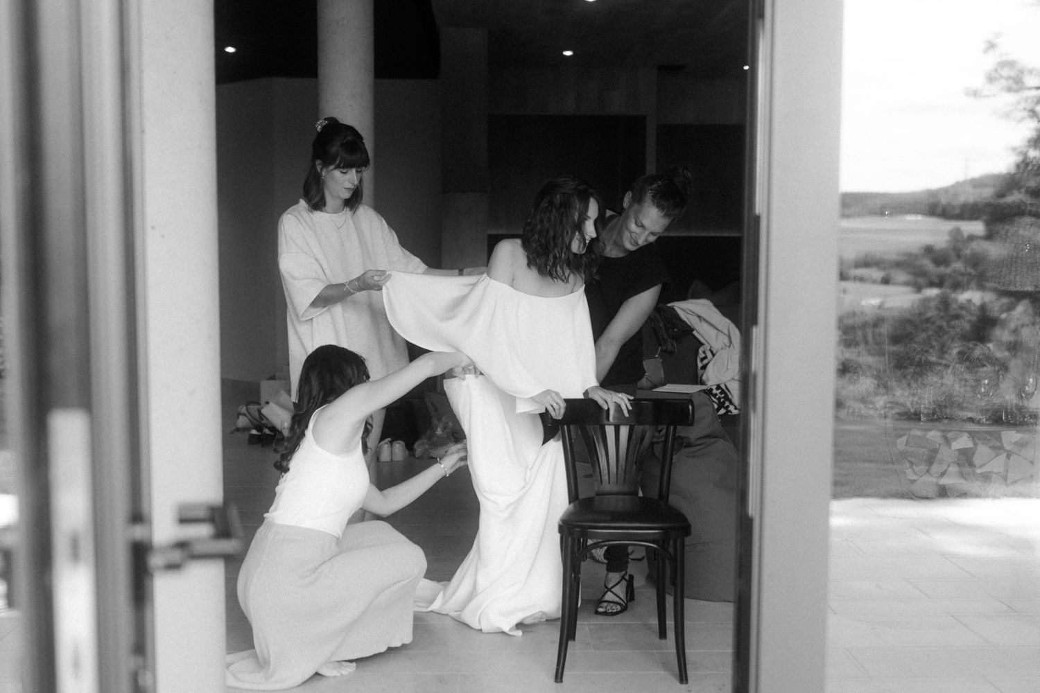 Black and white photo of bridesmaids helping with wedding dress preparations in a room.