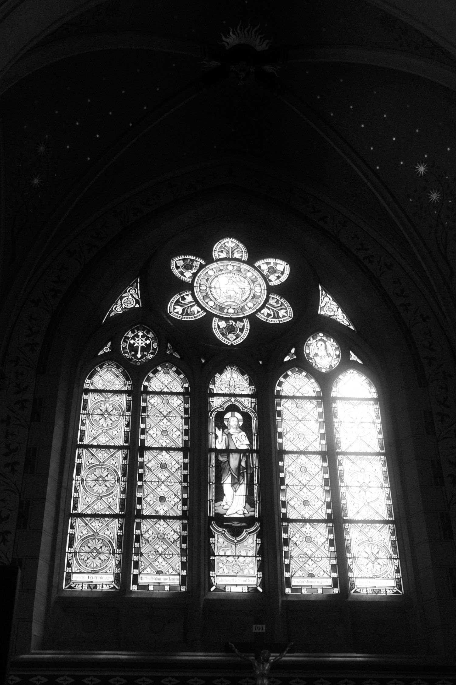 An ornate stained glass window in a gothic church features a floral pattern and religious imagery.