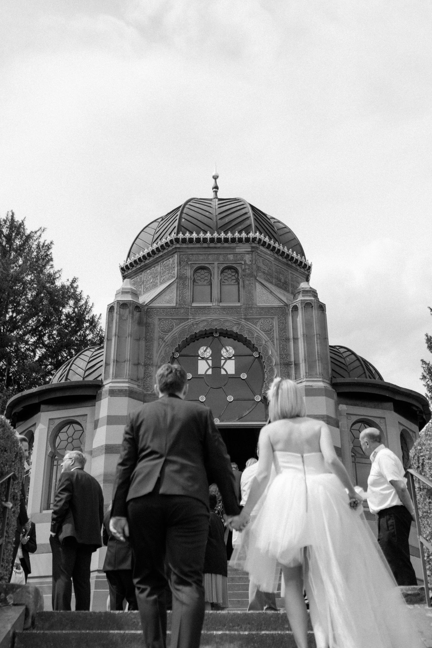 Wedding party ascending steps of a domed chapel in black and white photography.
