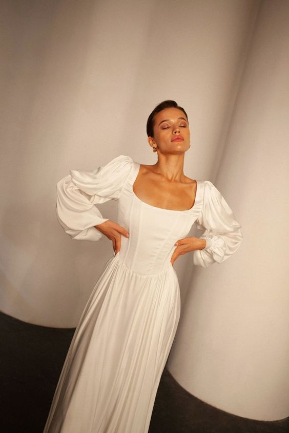 Dramatic white wedding gown with puff sleeves and fitted bodice in studio setting.