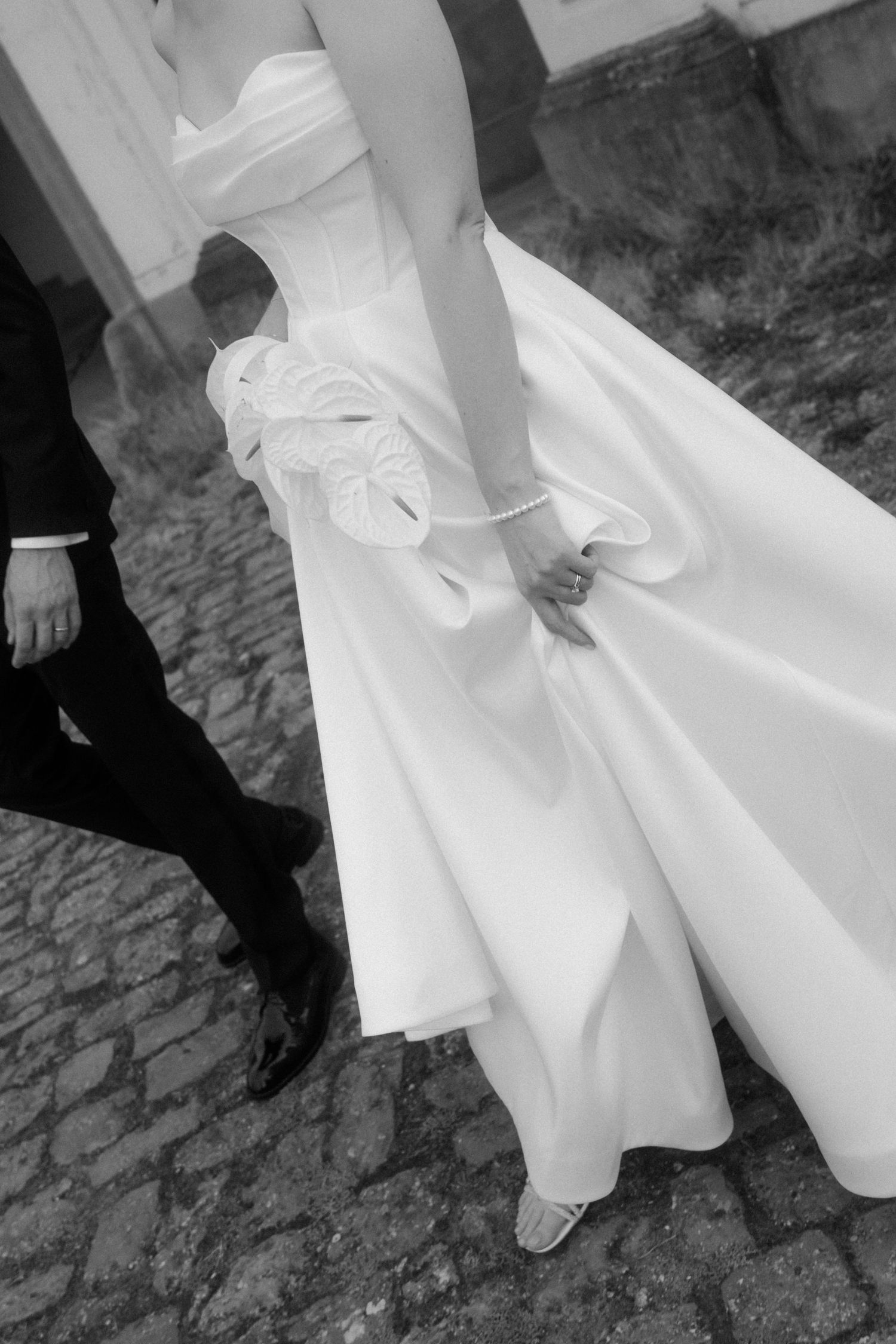 Close-up view of wedding dress details and formal shoes on a stone surface.