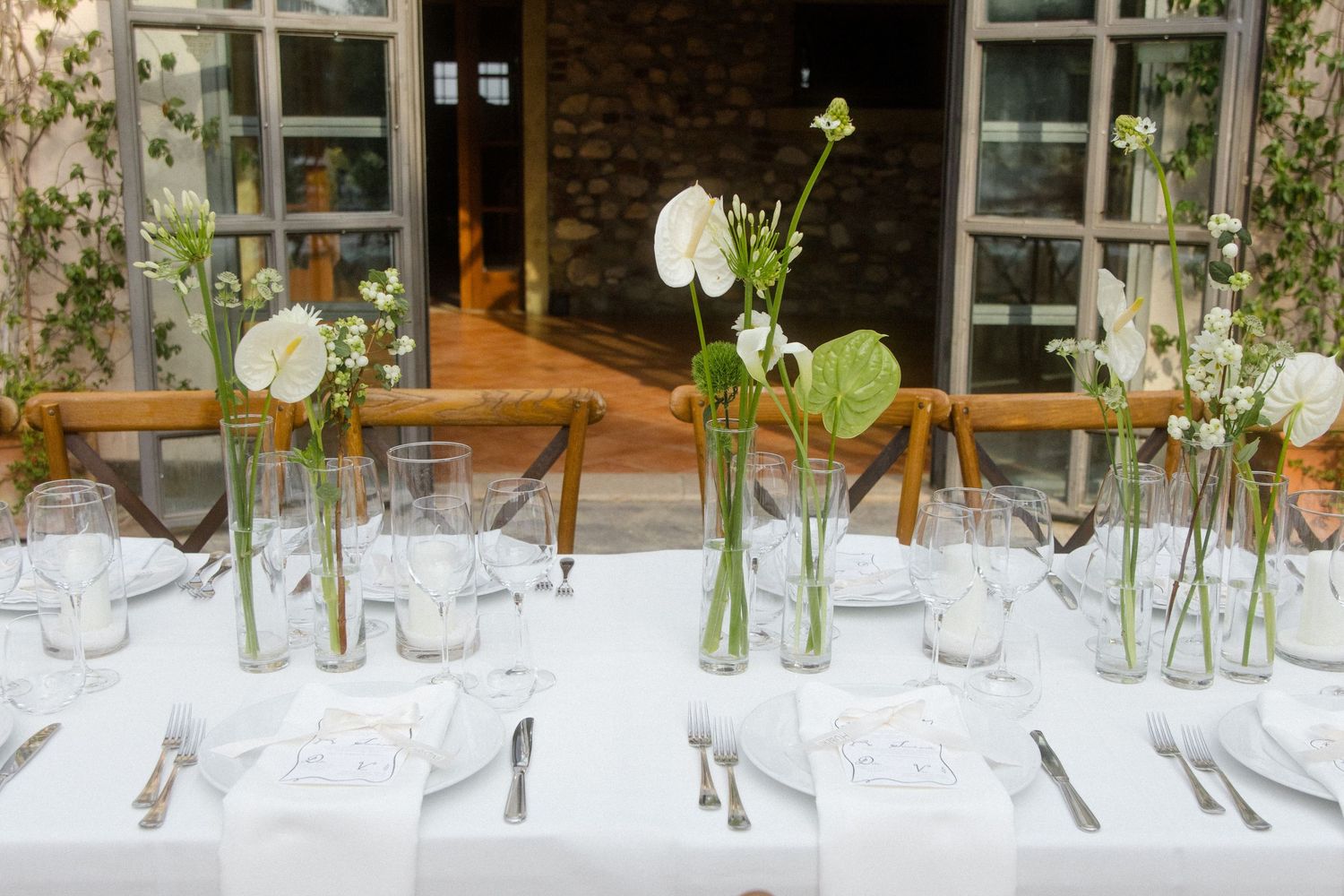 Wedding reception tables decorated with simple white linens and single stem flowers in glass vases.