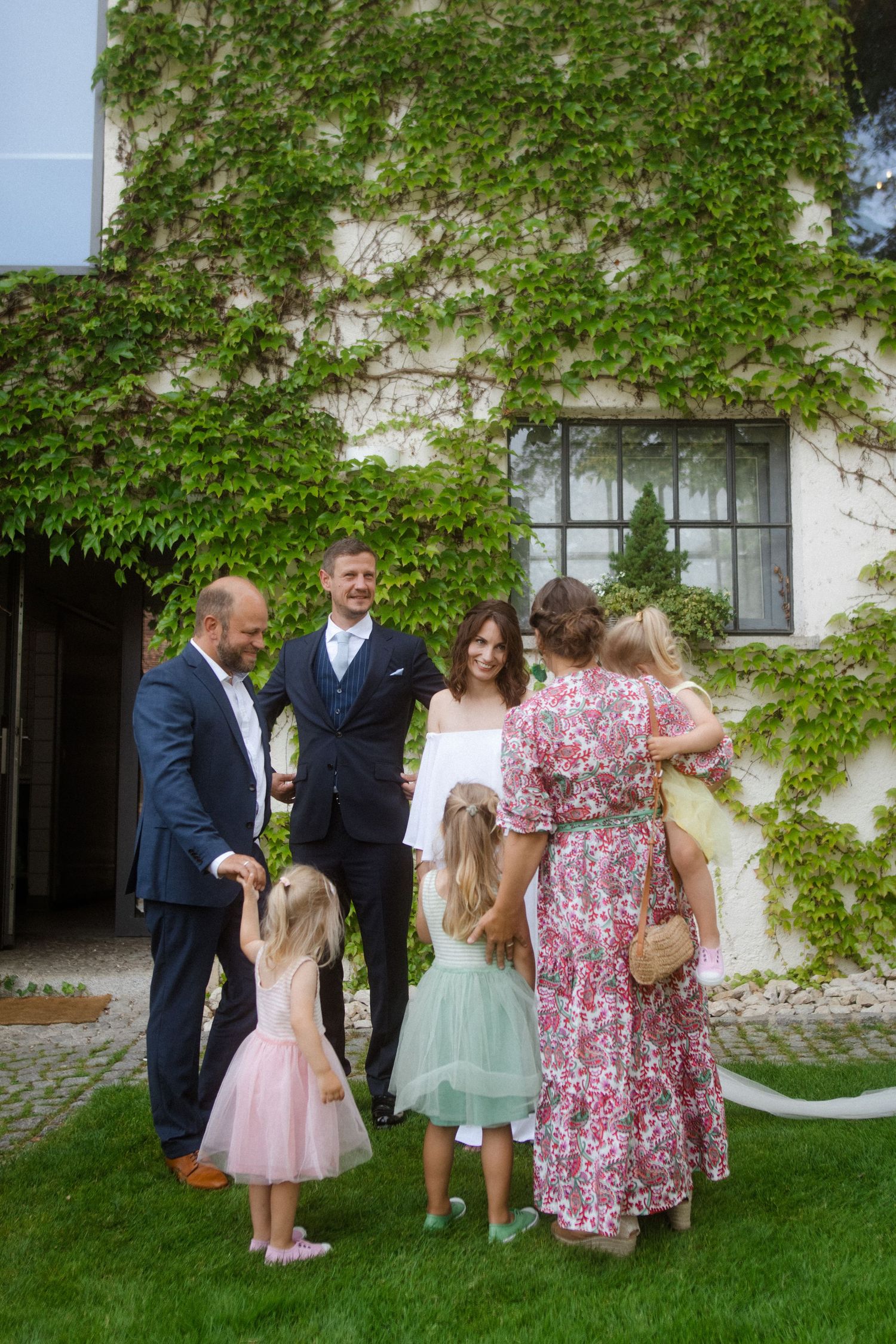 Wedding party gathers for photos in front of an ivy-covered building.