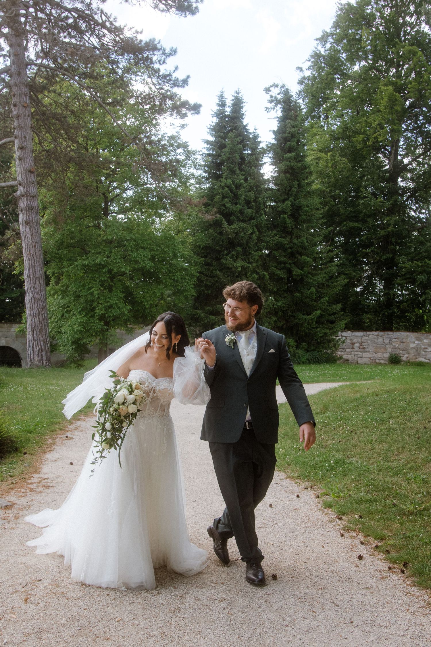 A couple walking along a garden path in formal wedding attire.