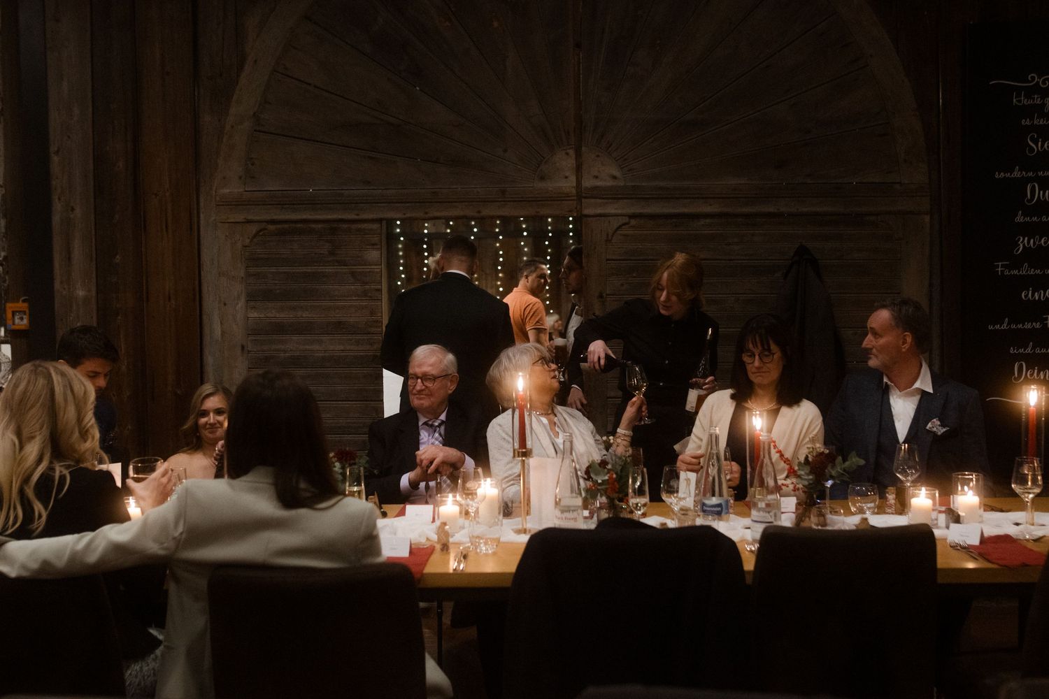 Wedding reception guests seated at long tables with candlelight and elegant decor in a dimly lit venue.