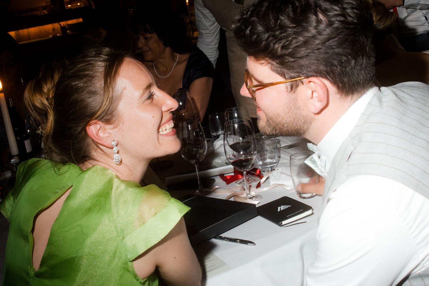 Couple sharing a romantic dinner at a restaurant, smiling at each other over glasses of red wine.