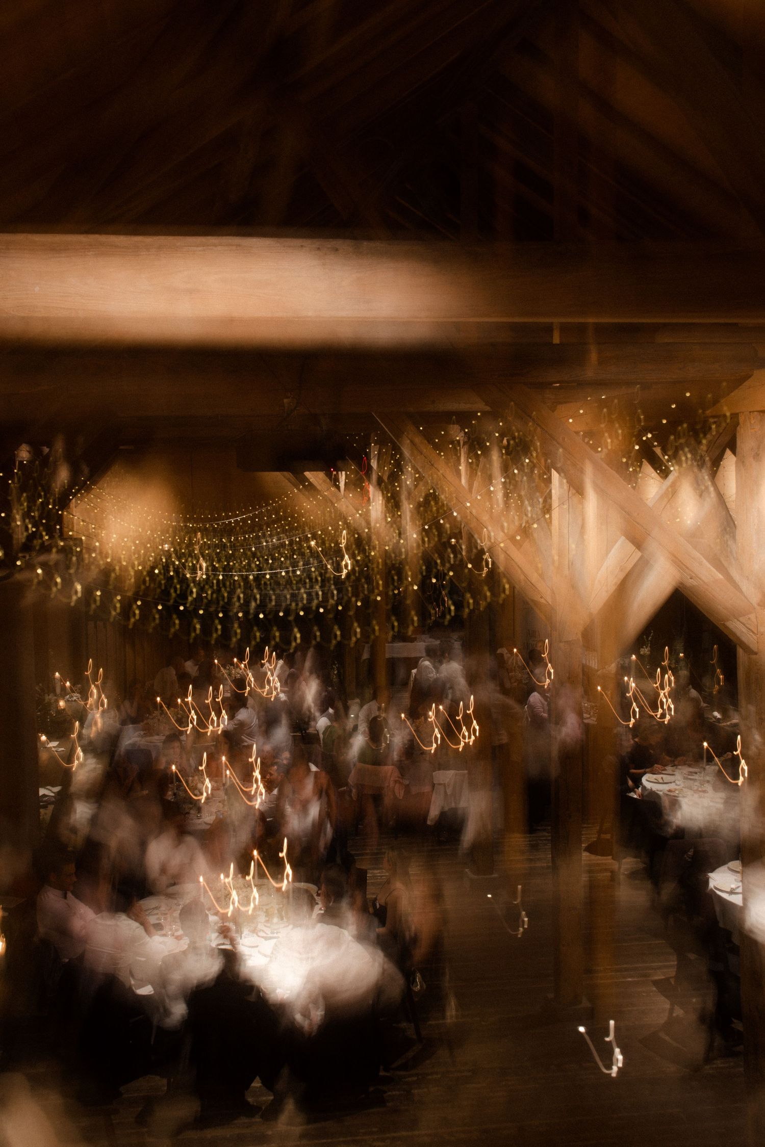 Blurred motion shot of wedding guests dancing under warm golden lights in a barn venue.