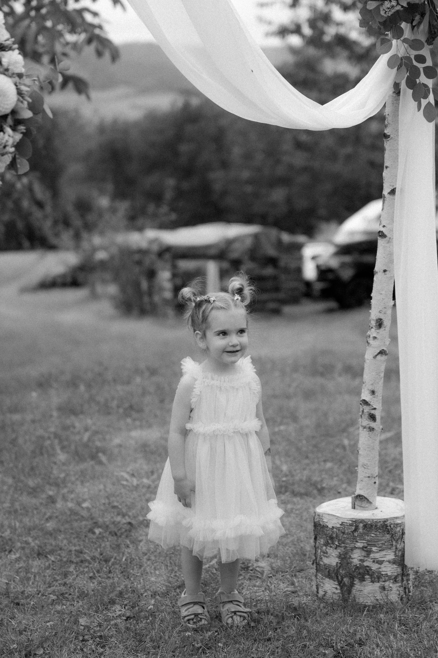 Black and white photo of a toddler in a white dress playing outdoors with decorative balloons.