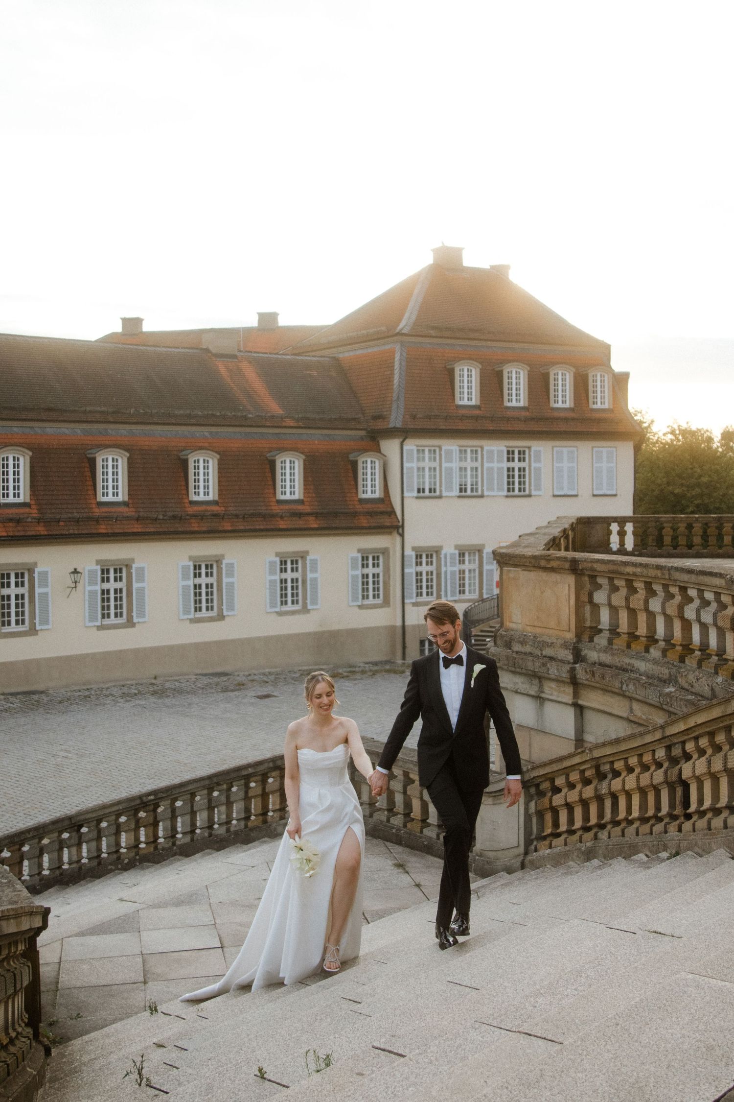 Newlyweds walking along an elegant stone terrace at sunset.