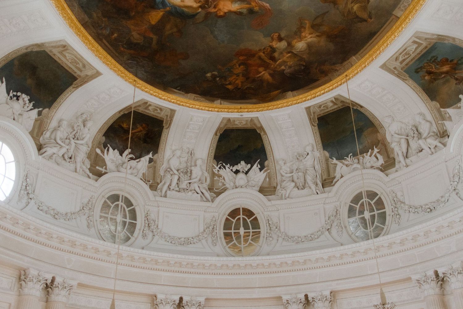 Ornate baroque ceiling with detailed frescoes and architectural elements in a grand hall.