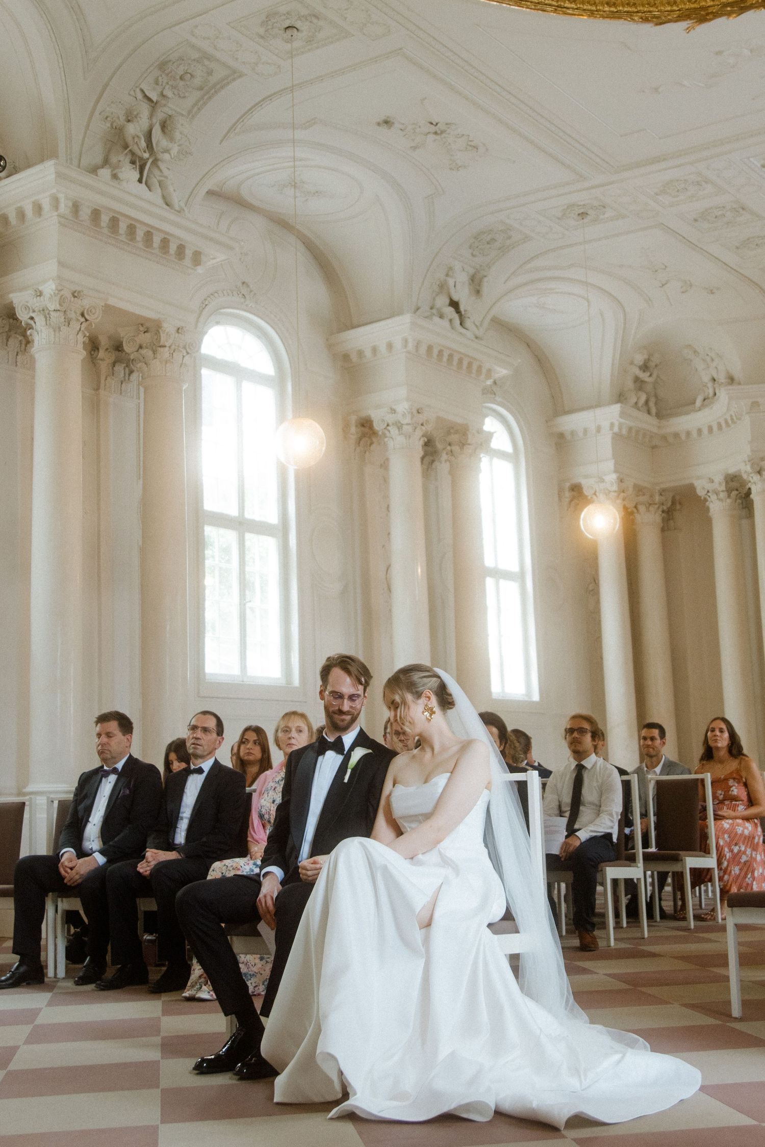 Wedding ceremony in a sunlit baroque hall with ornate architectural details.