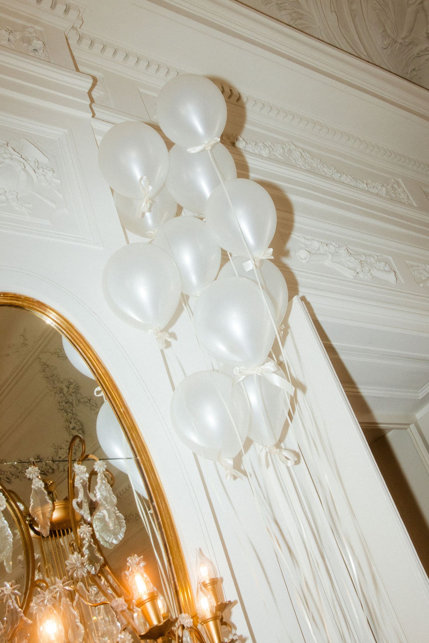 Elegant white balloons floating beneath an ornate ceiling with crystal chandeliers.