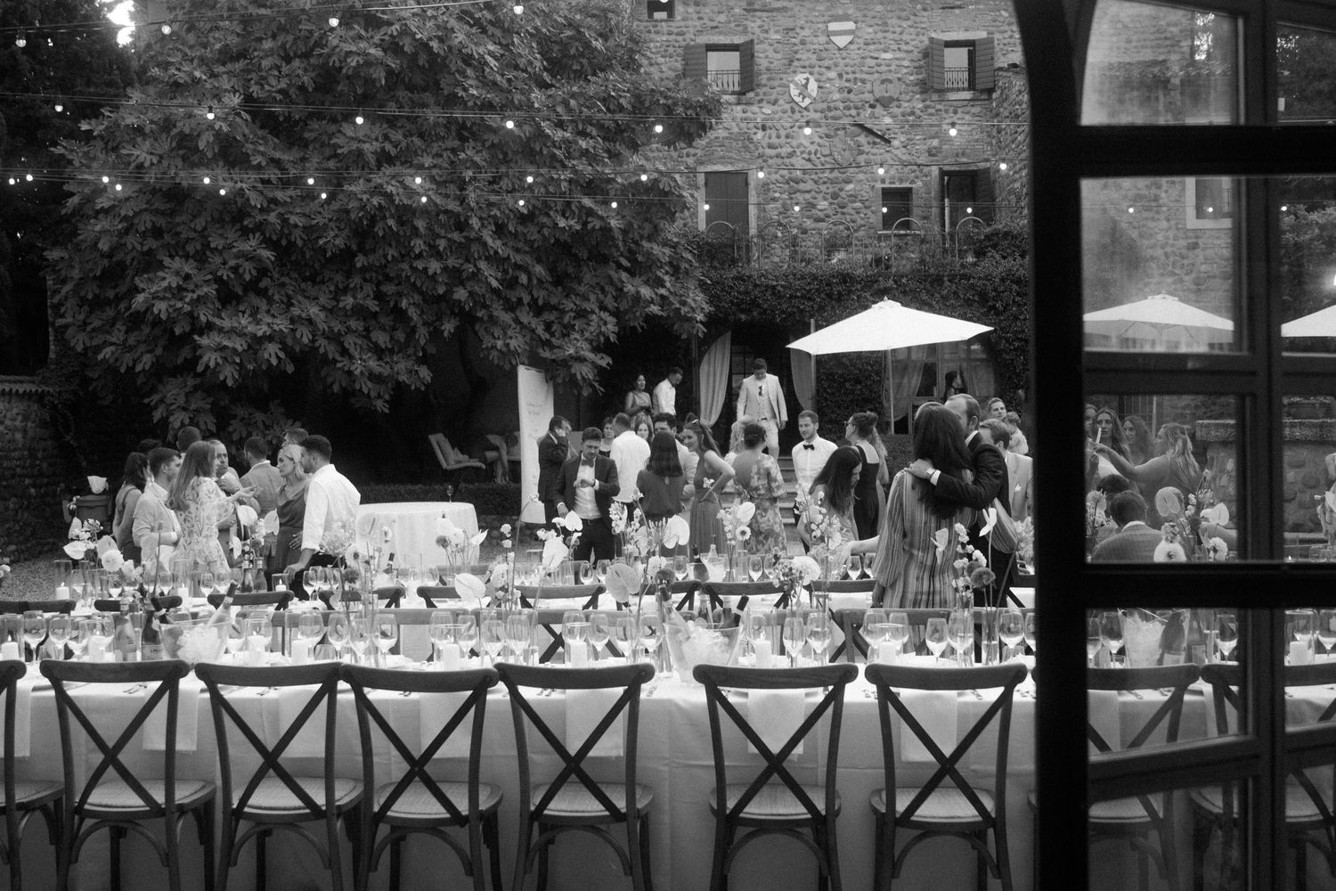 Black and white photo of an elegant outdoor wedding reception setup with long tables.