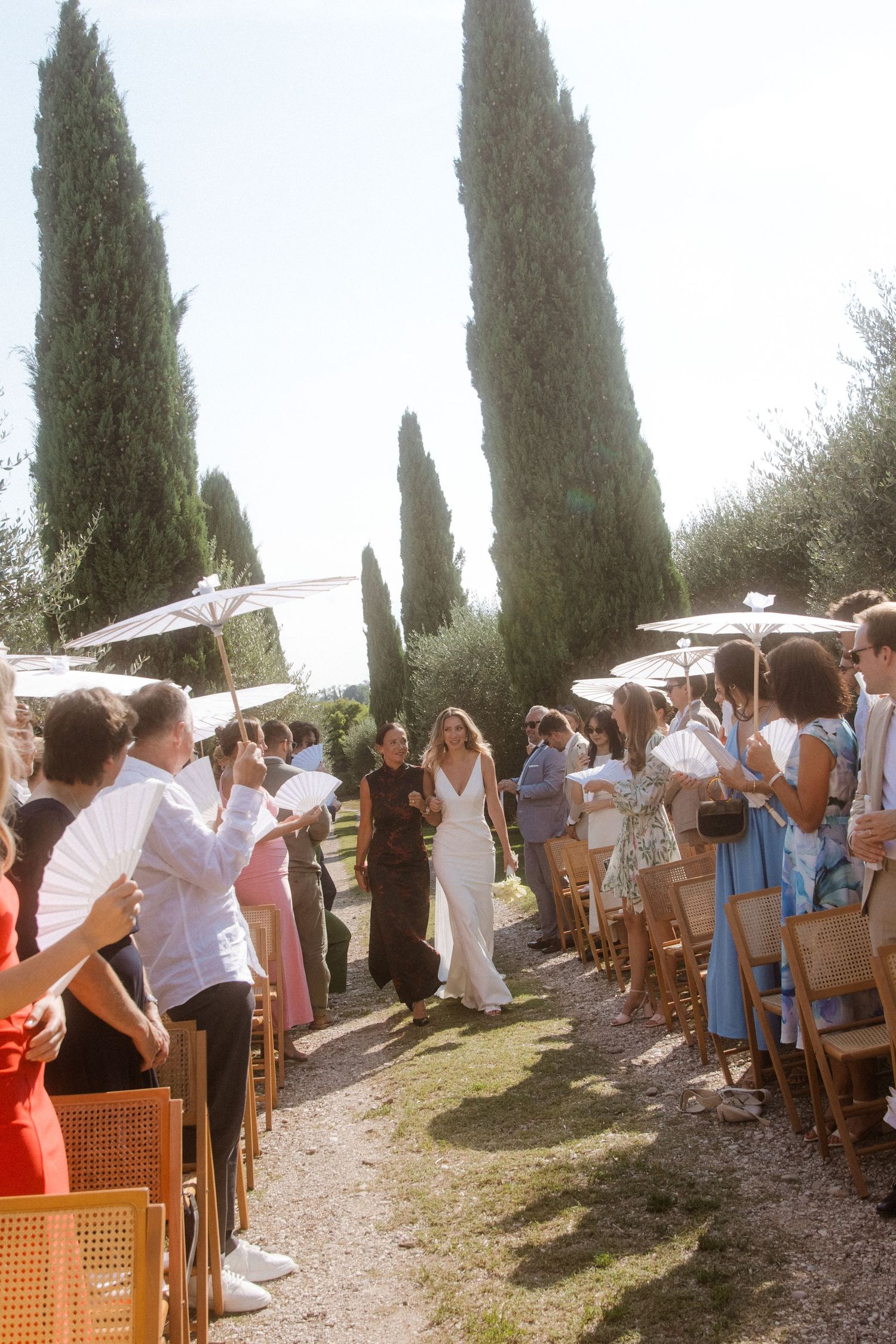 Outdoor wedding ceremony setup with white parasols and cypress trees in a Tuscan garden setting.