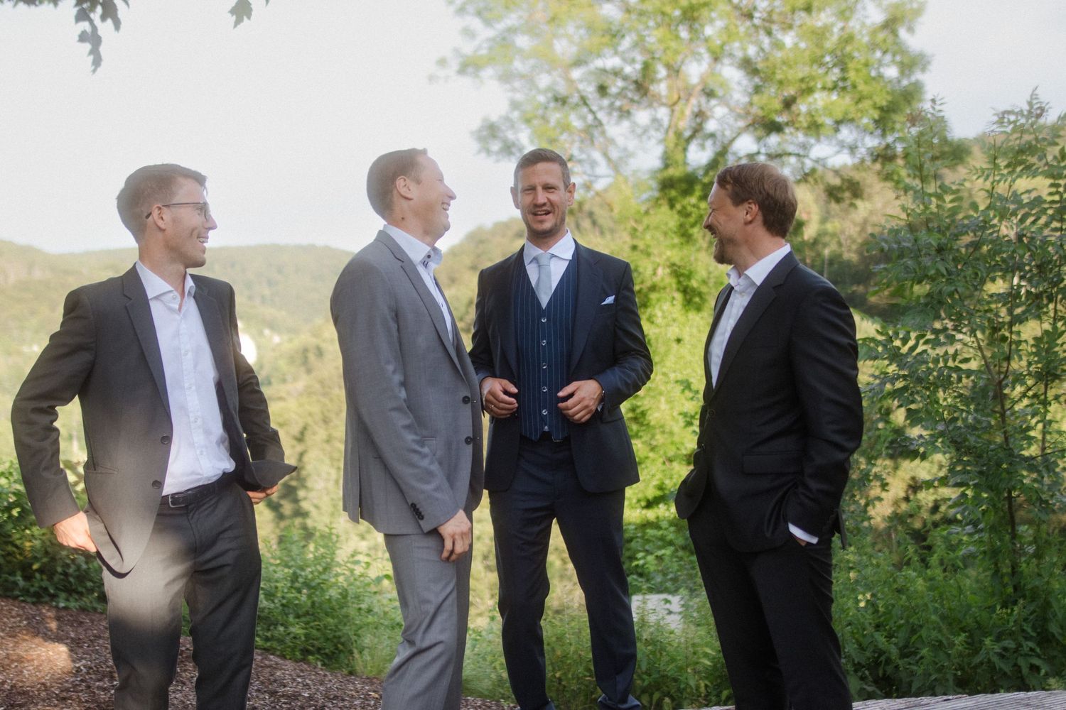 Four men in formal suits having an animated conversation outdoors with sun flare.