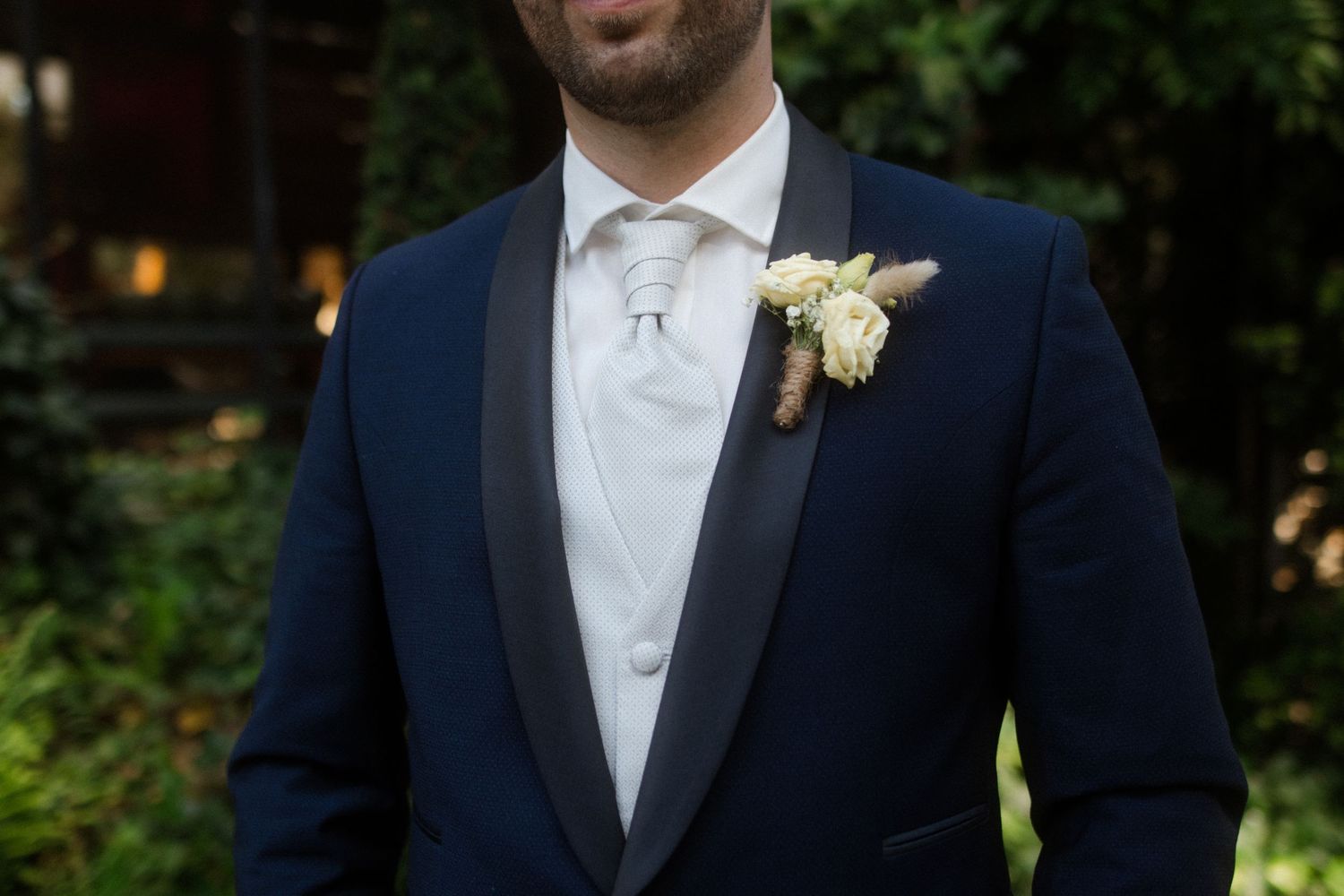 Close-up detail of a groom's navy blue tuxedo with white boutonniere.