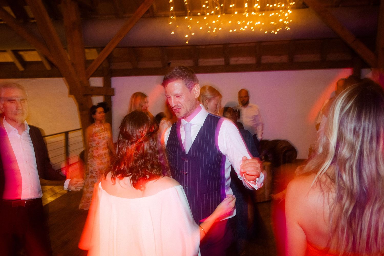 Blurred motion capture of dancing guests at a reception with warm lighting.