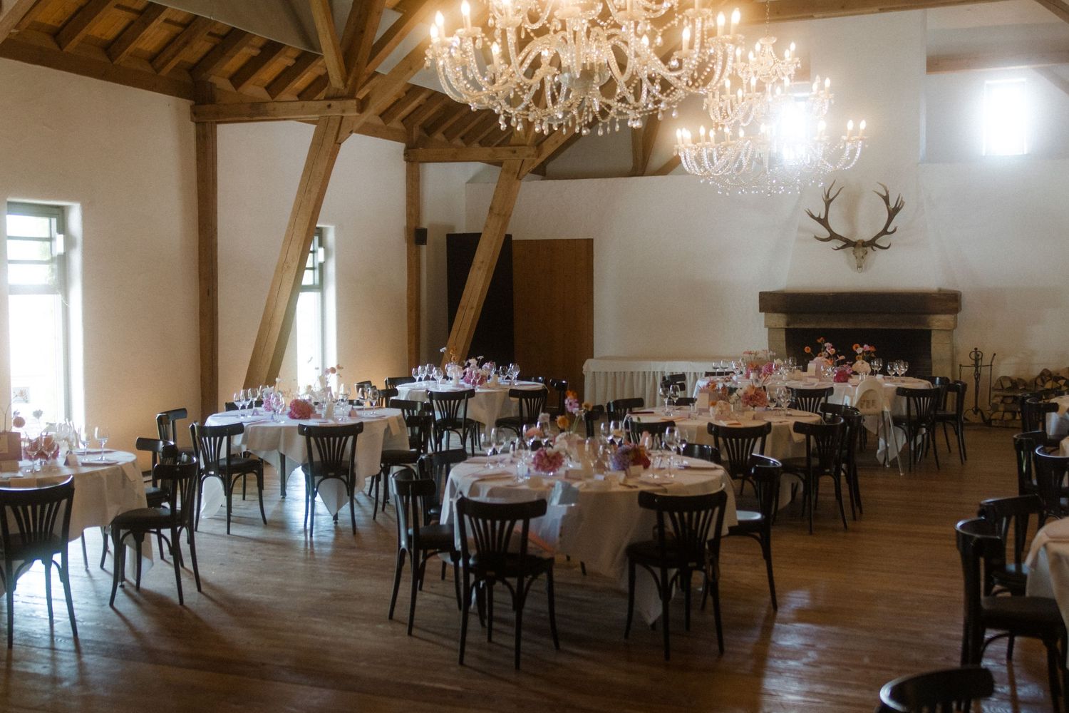 Wedding reception venue with crystal chandeliers and rustic wooden beams overhead.