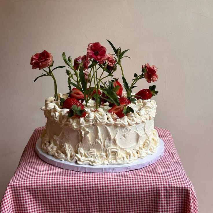 Single-tier white wedding cake topped with red carnations on pink gingham tablecloth.