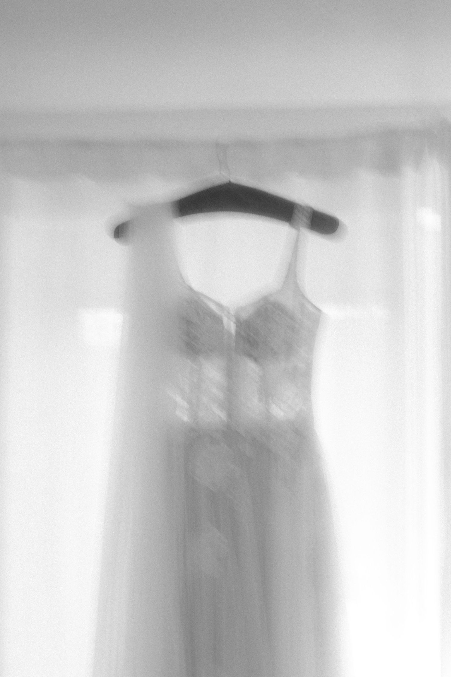 A dreamy, soft-focus black and white image of a white wedding dress hanging on a clothes hanger.