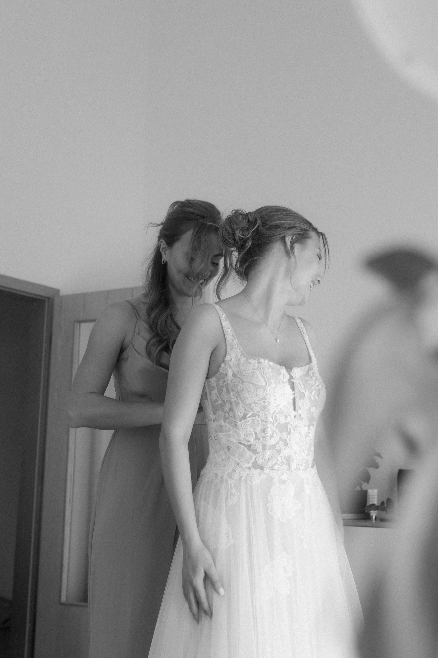 A black and white photograph of a bridal dress being fitted in an intimate getting-ready moment.