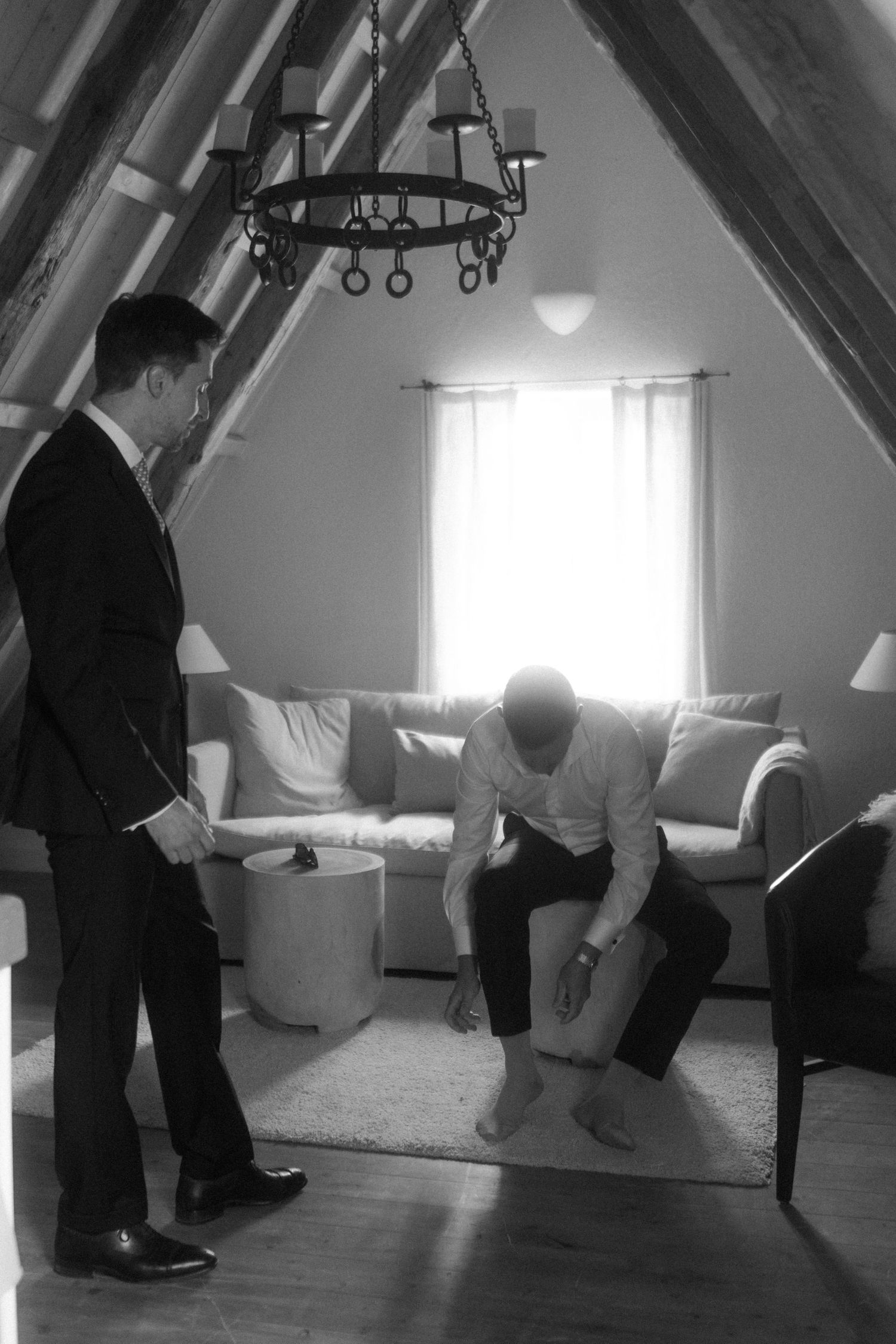 Two people in an attic room with slanted ceiling and chandelier.