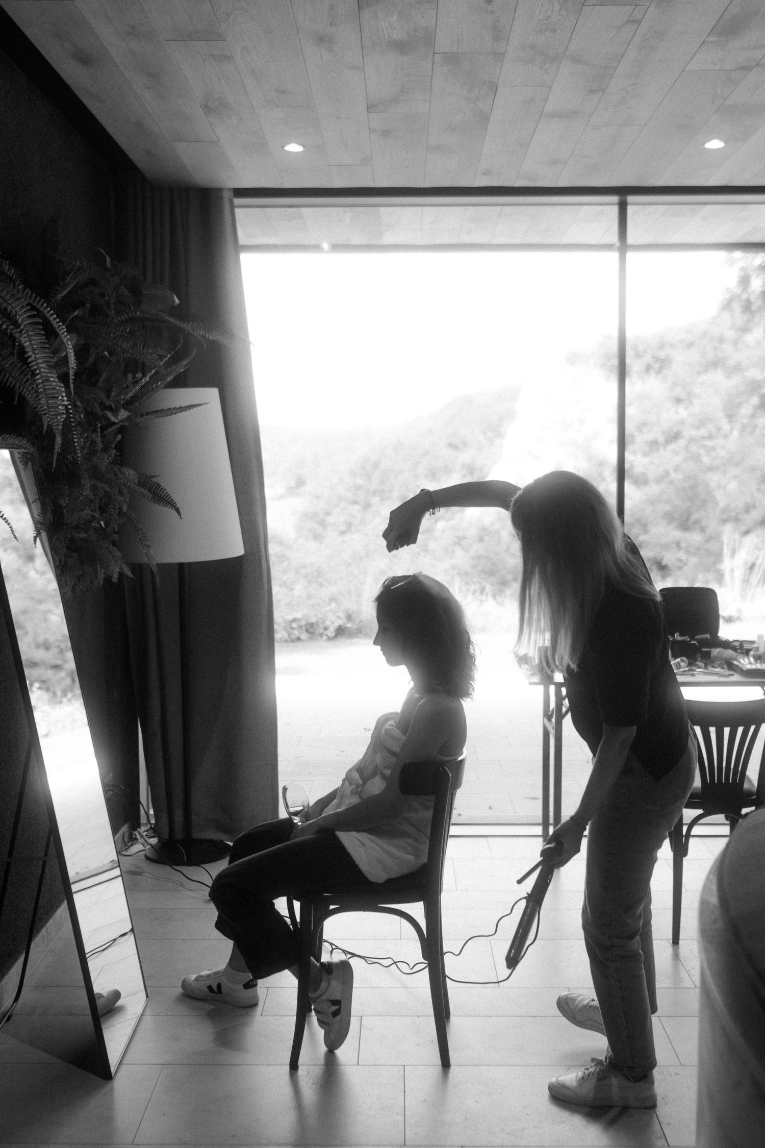 Black and white image of wedding day hair styling preparation by a window.