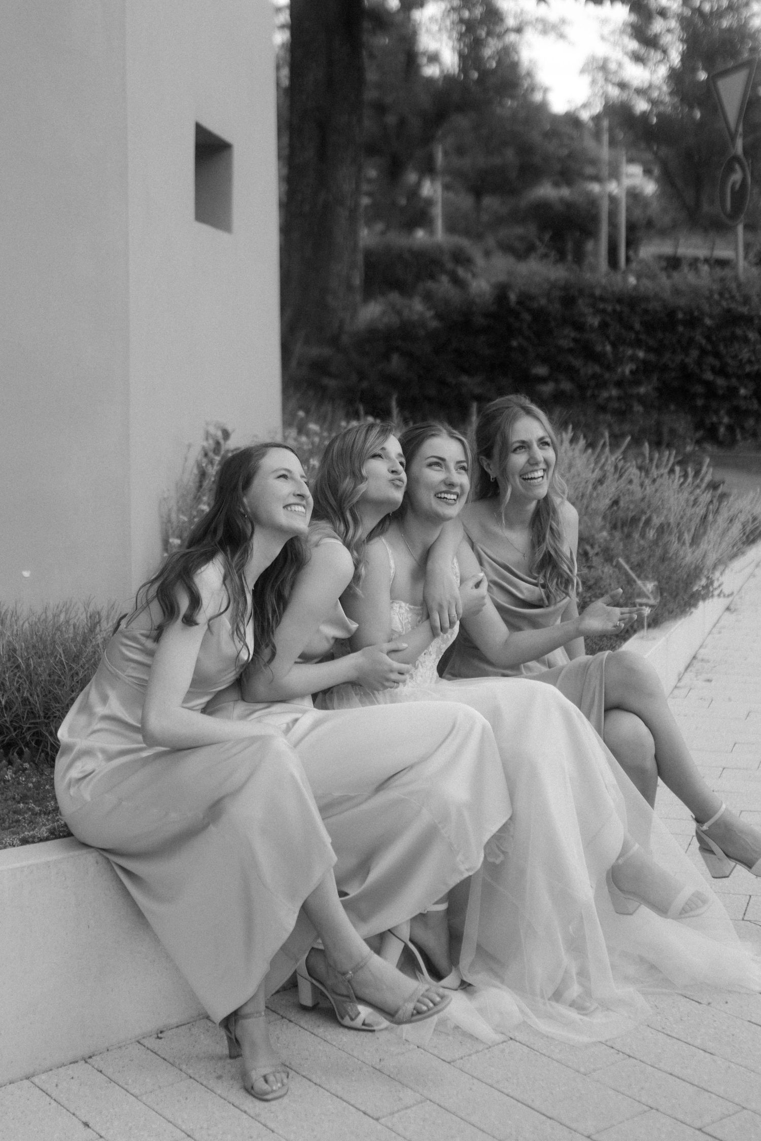Black and white photo of bridesmaids laughing together while sitting outdoors.