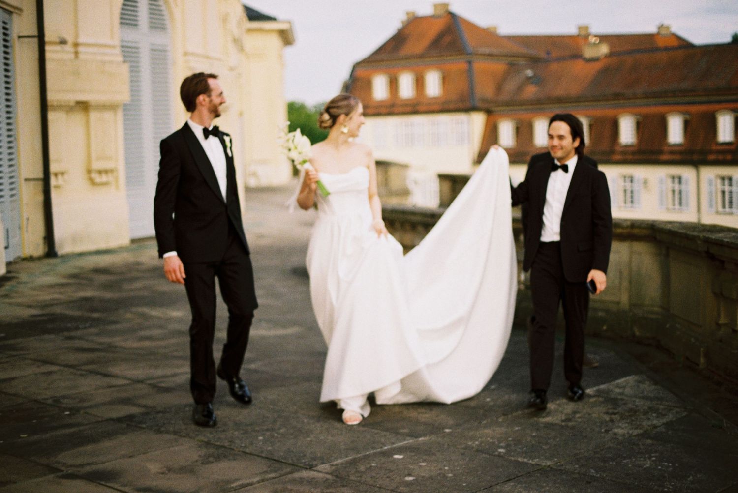 A panoramic series of wedding photos showing a couple walking along a building exterior at sunset.