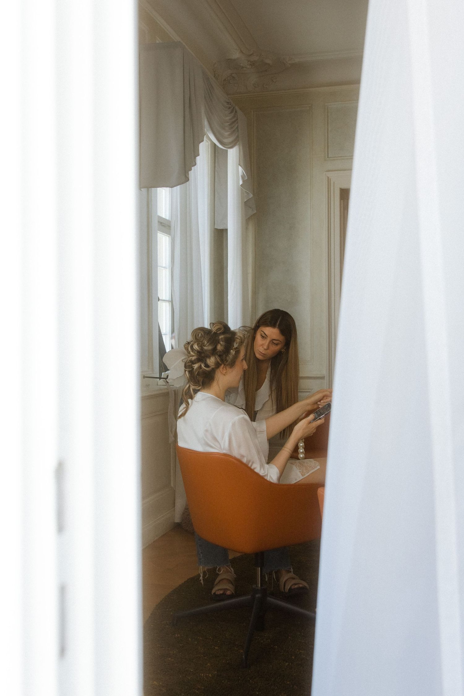 Elegant white room with mirrors and orange salon chairs reflecting natural light.