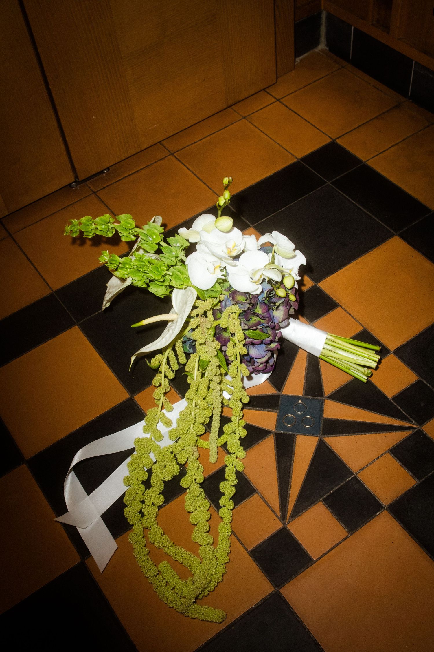Green and white floral bouquet lying on a checkered floor under dramatic lighting.