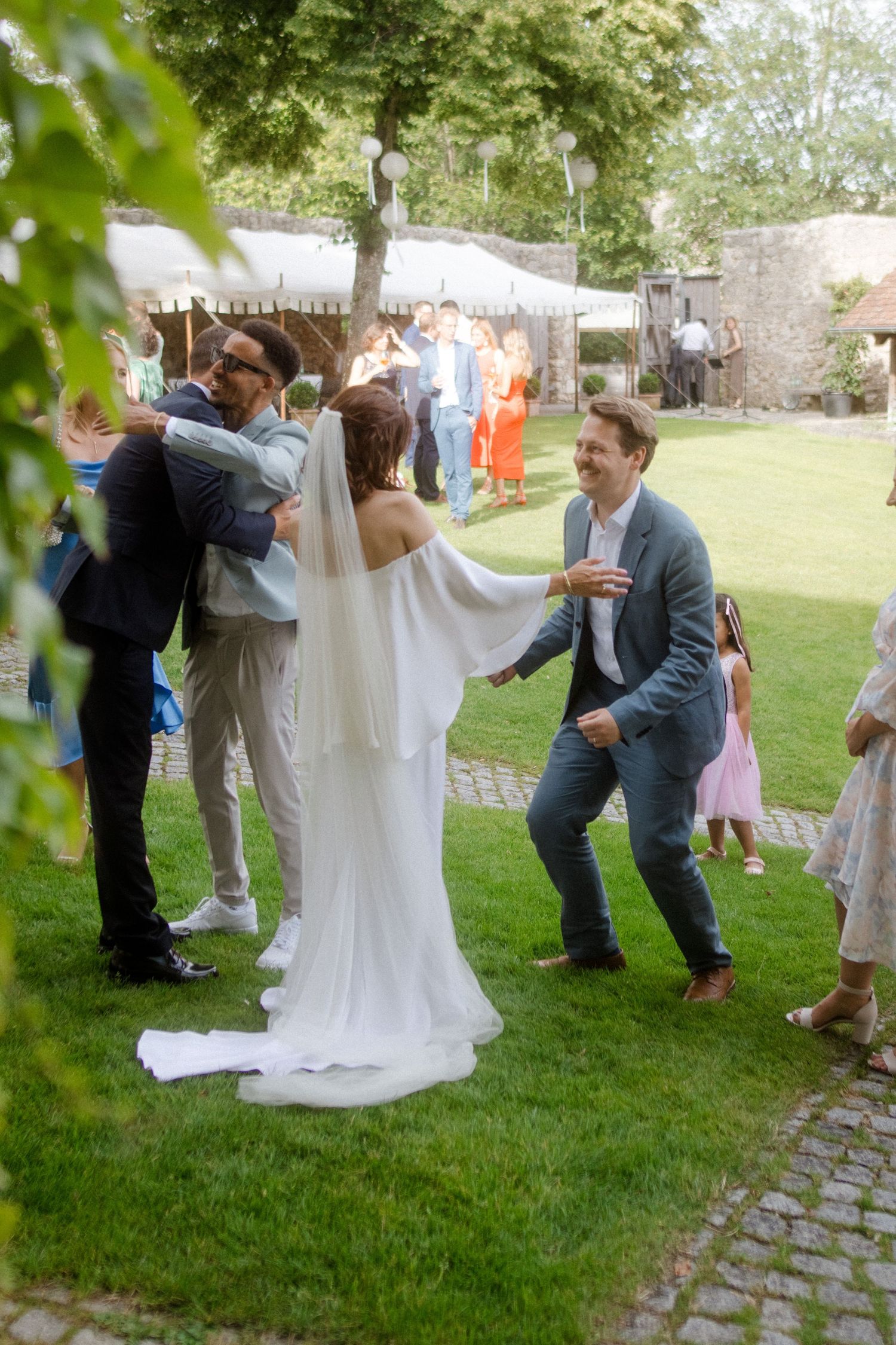 Joyful wedding celebration with guests dancing and embracing in garden setting.