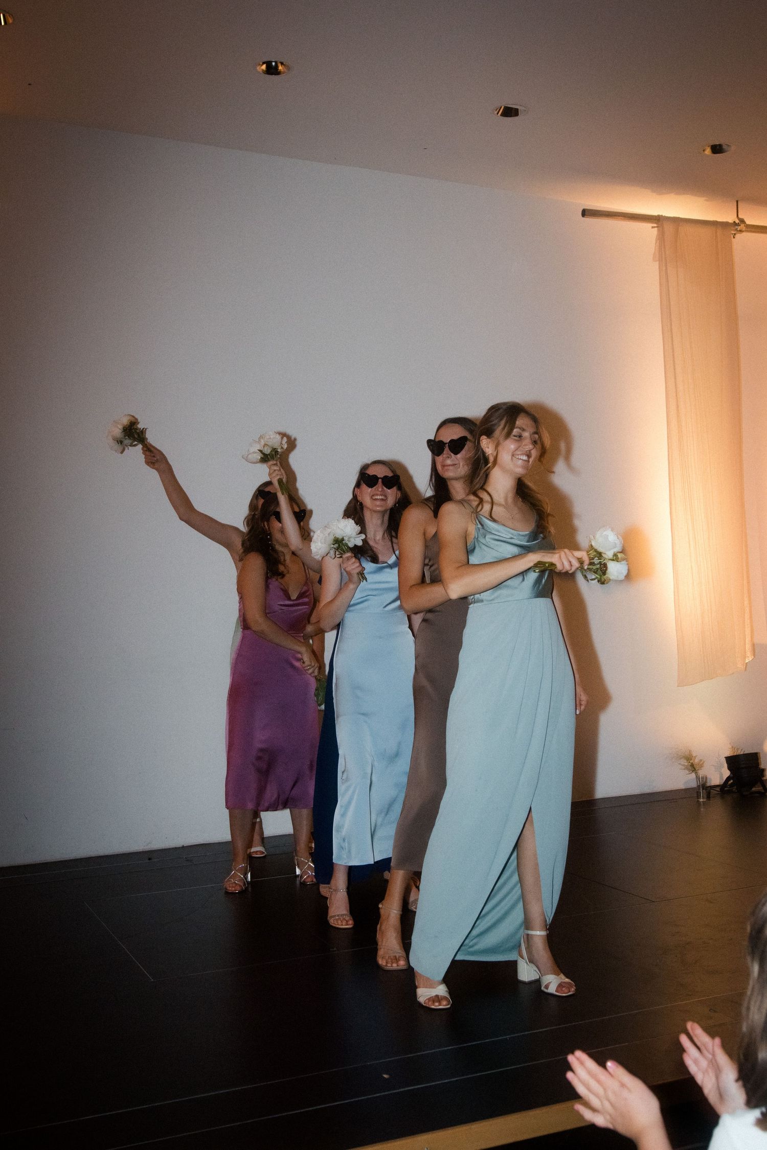 Bridesmaids in coordinating dresses strike a fun pose while wearing sunglasses.