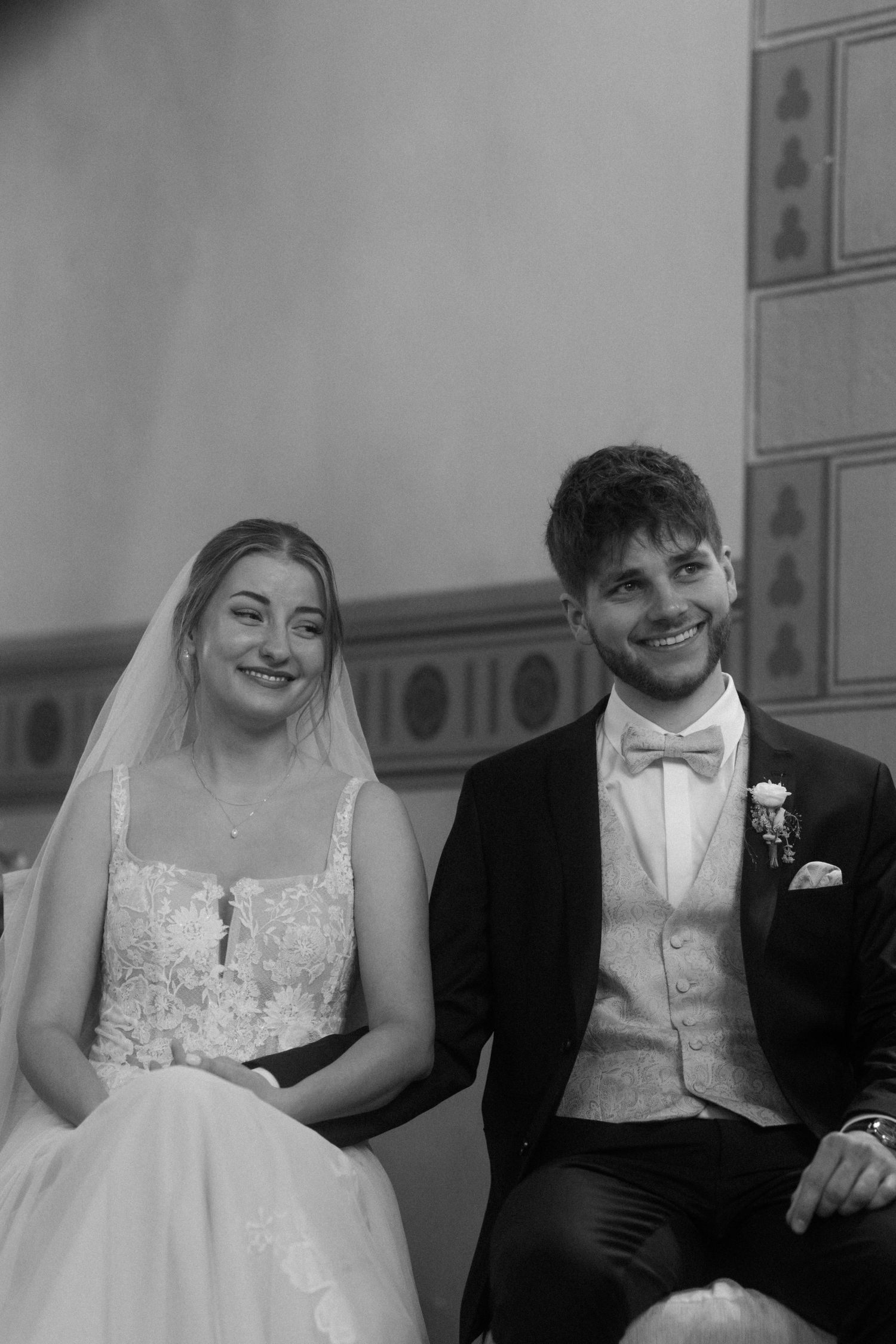 A wedding couple sits together in formal attire during their church ceremony.