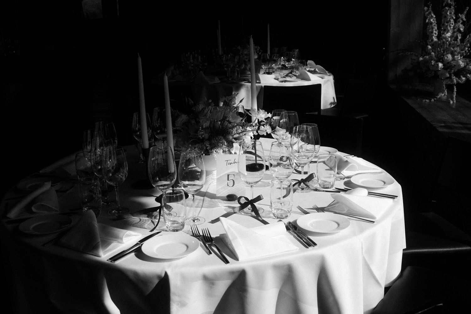 Black and white photo of a formal wedding banquet table set with plates, glasses, and candles.