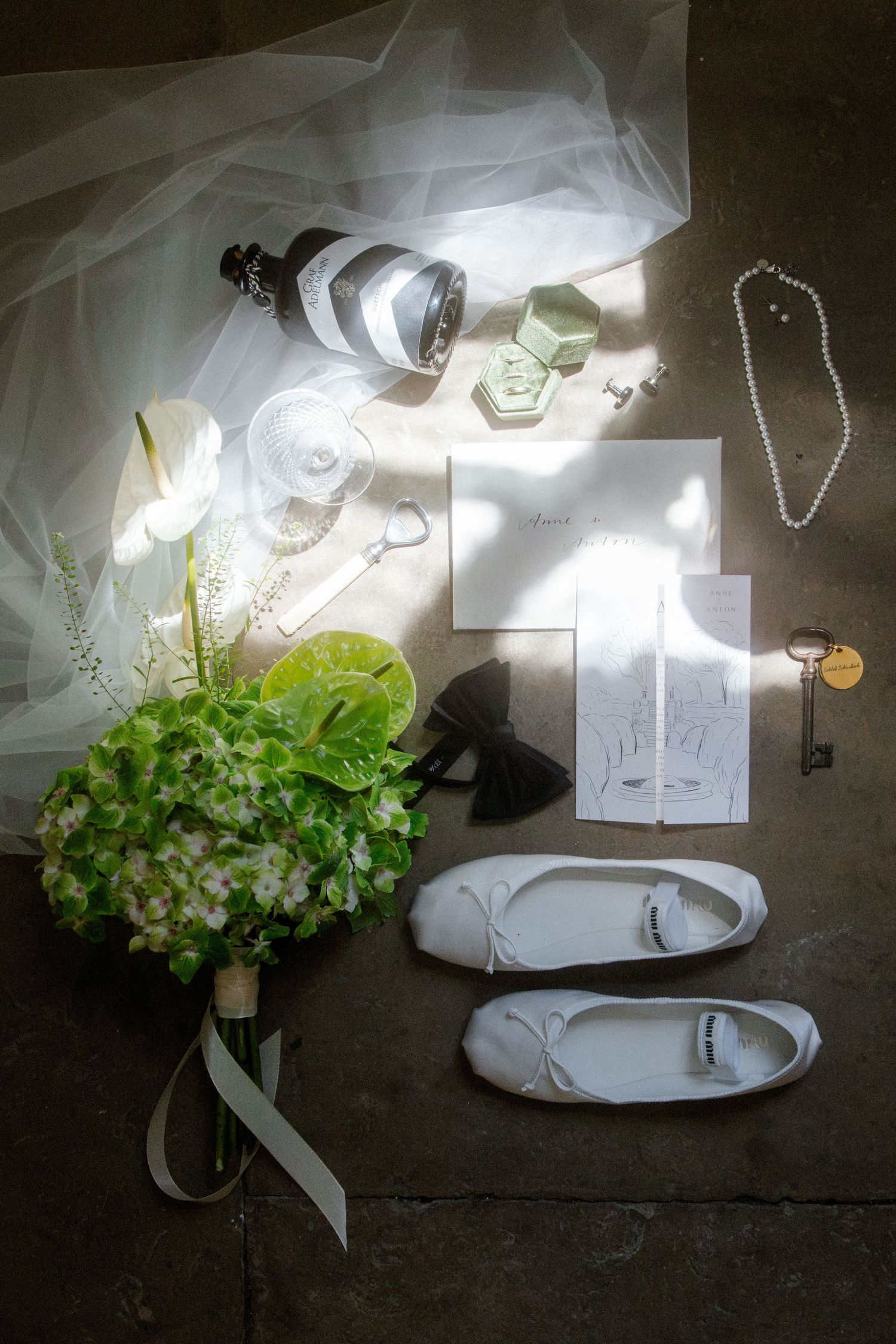 Flat lay of bridal accessories including white ballet flats, green hydrangea bouquet, pearl necklace, veil, and wedding stationery.
