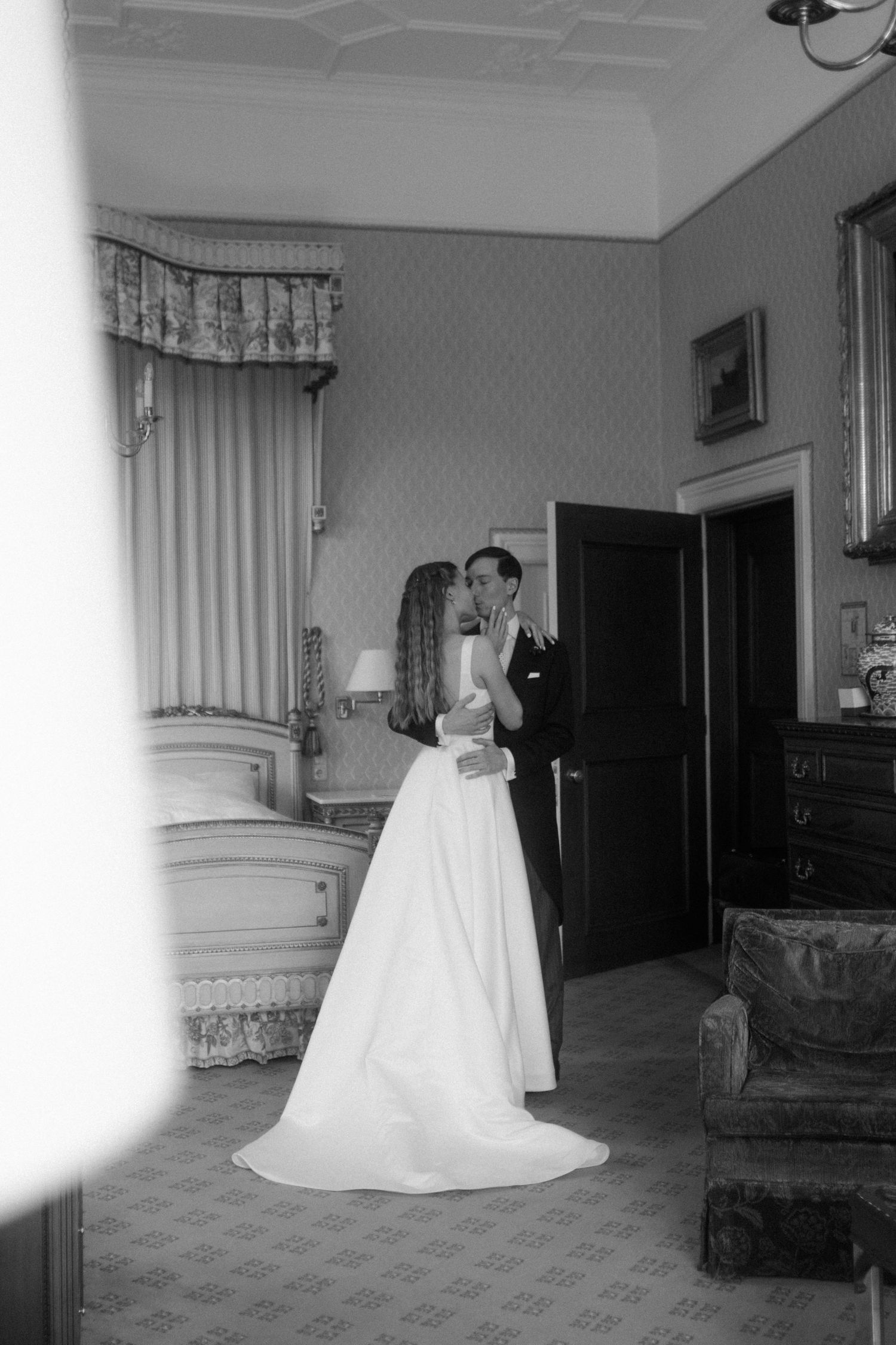 Black and white photo of newlyweds in an ornate room with antique furniture and flowing curtains.