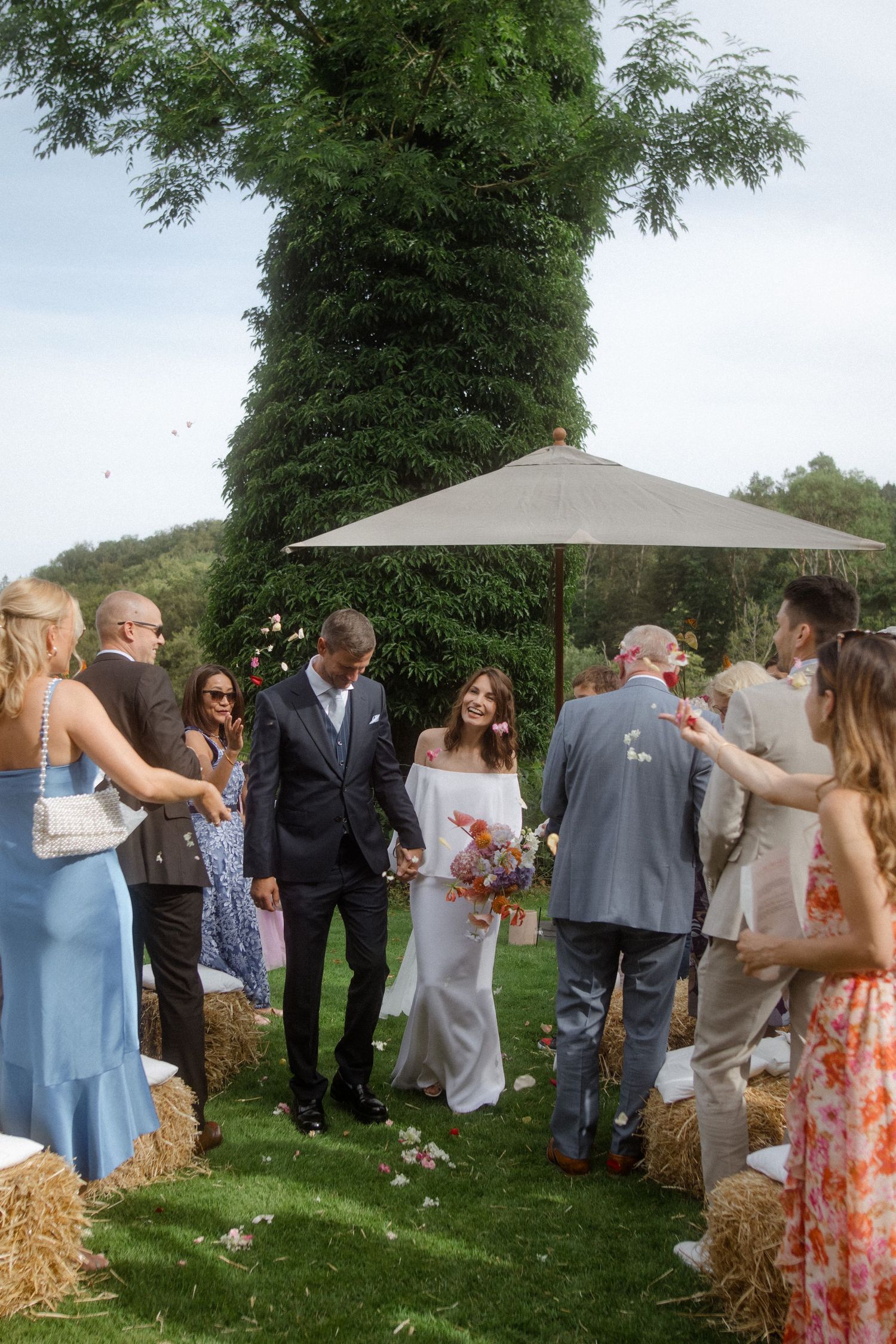 Wedding guests gather around hay bales during an outdoor garden reception.