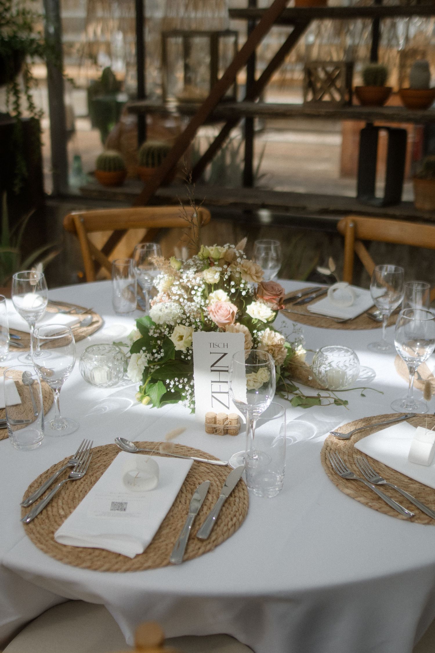 An elegant table setting with floral centerpiece, woven chargers, and wine glasses on a white tablecloth.