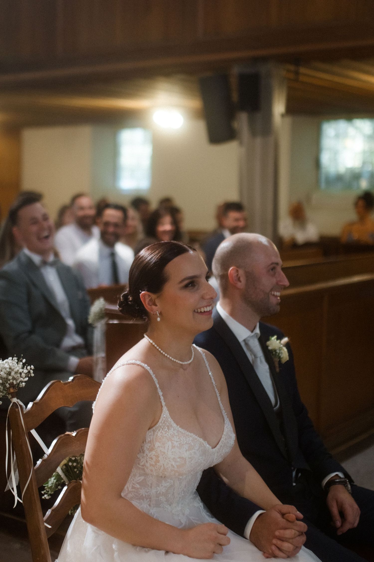 A couple seated in wooden church pews sharing a joyful moment during their wedding ceremony.