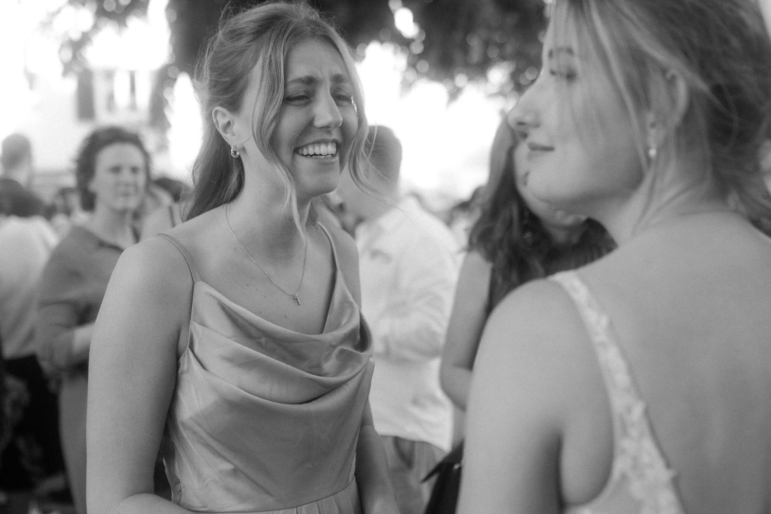 Black and white candid moment of laughter between guests at wedding reception.