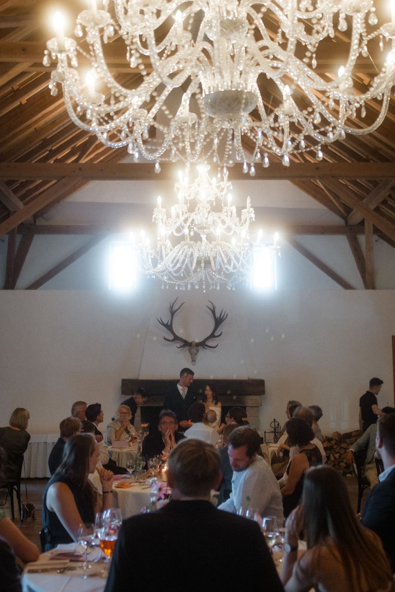 Grand wedding dinner under ornate crystal chandeliers with antler decor in rustic reception hall.